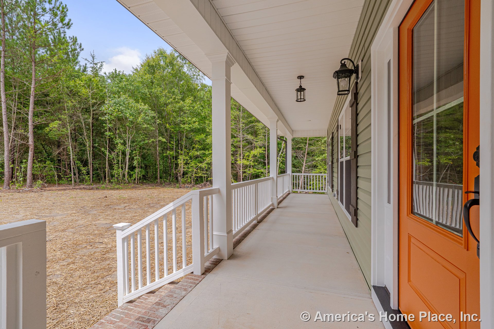 Covered front porch with white railings and columns, orange entry door, green siding exterior, brick step, black outdoor lanterns, and ceiling lighting fixture.