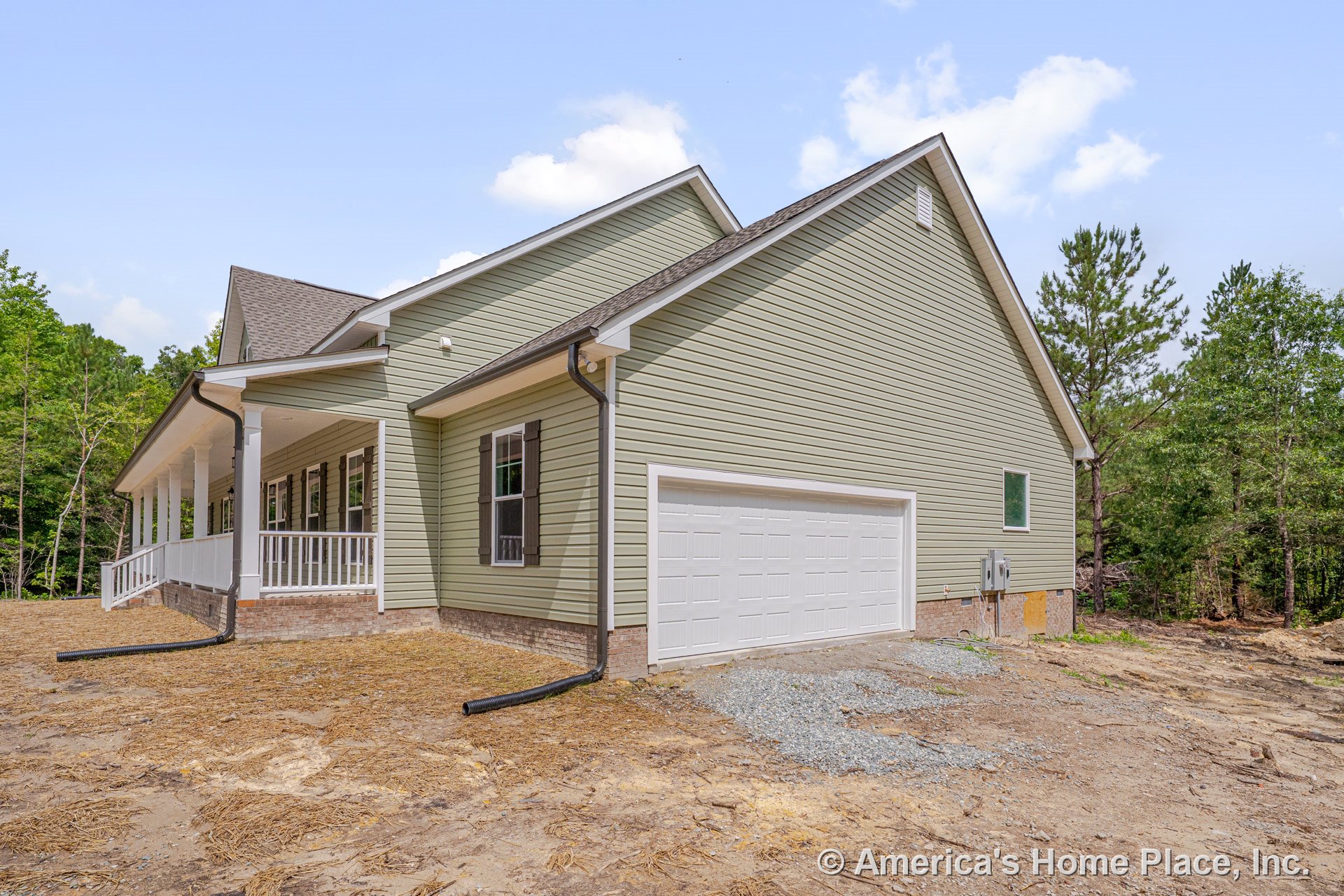 Light green vinyl siding exterior with attached two-car white garage door, covered front porch featuring white railings and columns, brick foundation trim, dark window shutters