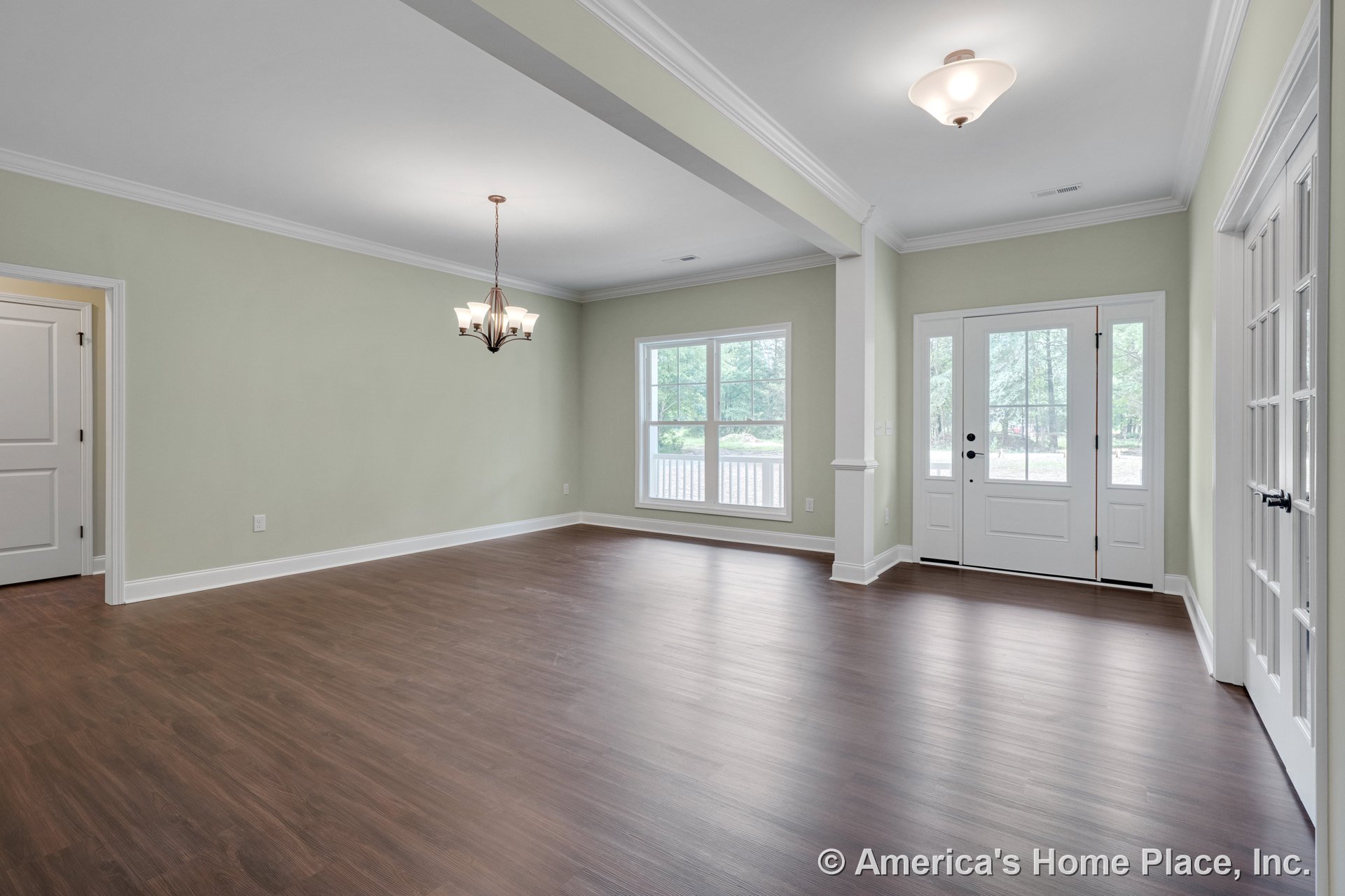 Double front doors with glass panels and transom window open to foyer with wood-look plank flooring, crown molding, white trim and baseboards, large dining area window, and two