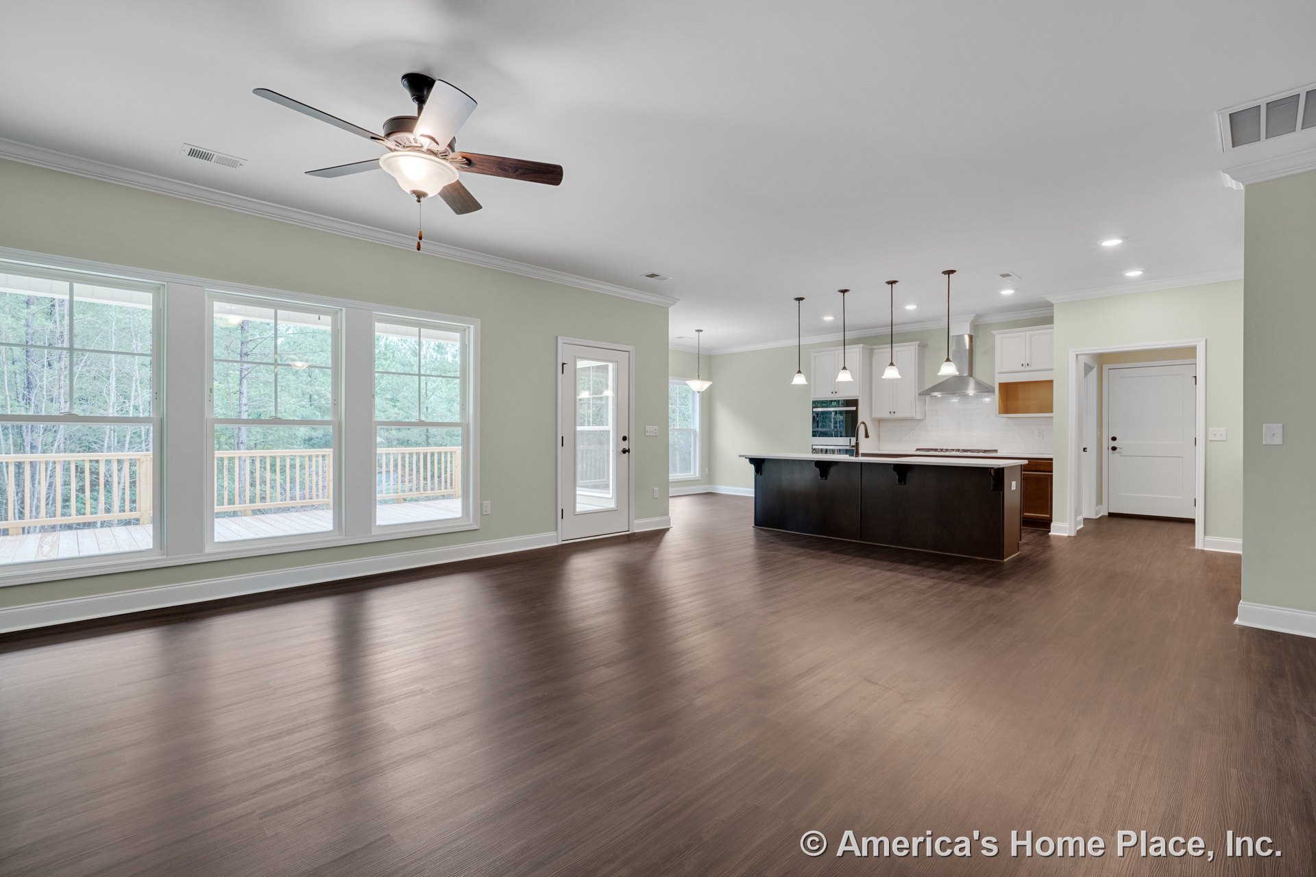 Open-concept living area with three-panel windows, dark wood flooring, kitchen island beneath pendant lights, white cabinetry, tile backsplash, ceiling fan with light fixture