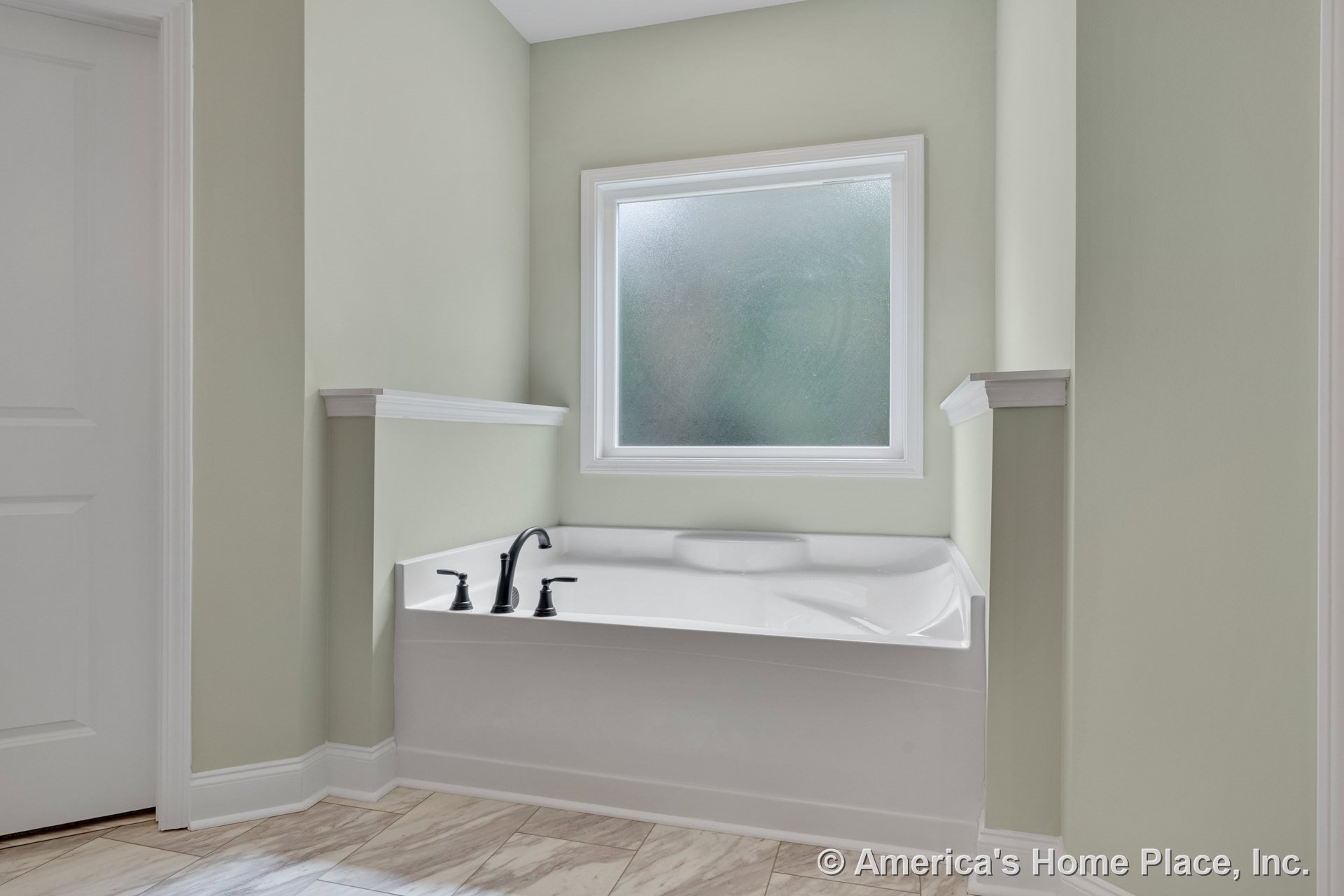Built-in corner soaking tub with matte black fixtures set beneath a frosted window, surrounded by soft green walls, white trim, and tile flooring.