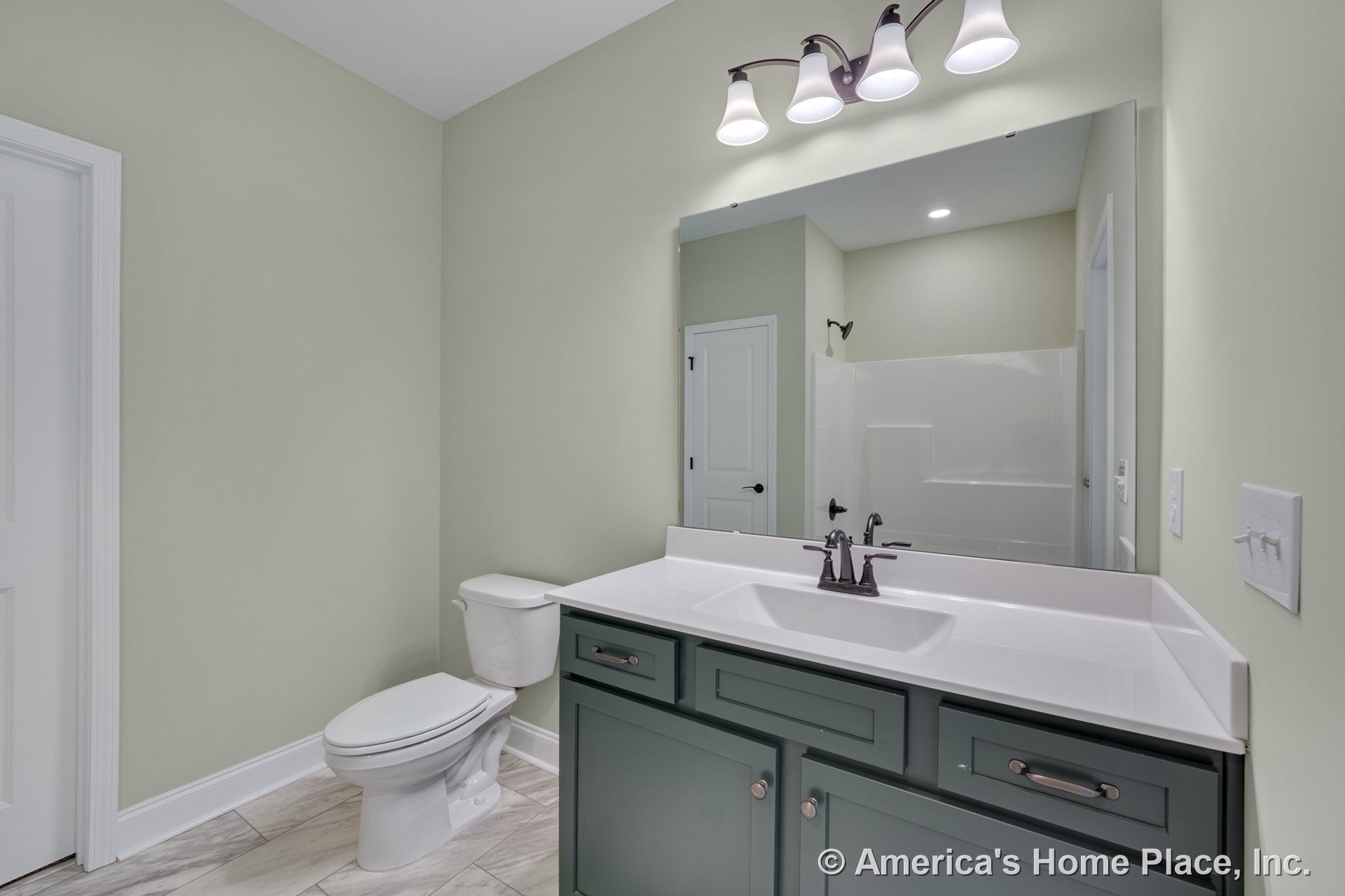 Single-sink vanity with green cabinetry and white solid surface countertop, large wall mirror with three-light fixture above, tile flooring, and white toilet.