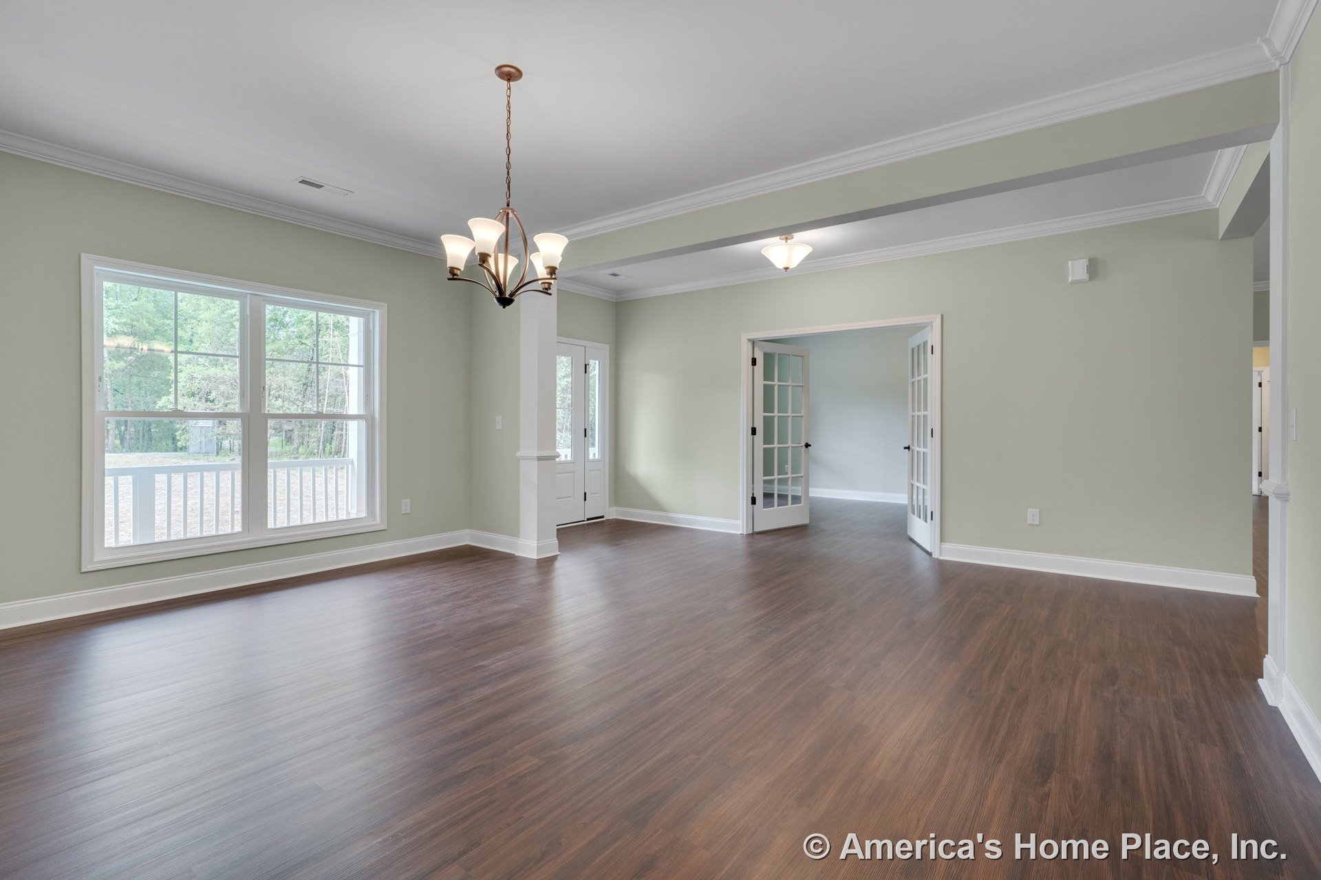 Wide plank wood flooring in a spacious living area with large double windows, French doors, white crown molding, built-in ceiling lights, entry door with sidelights, and neutral