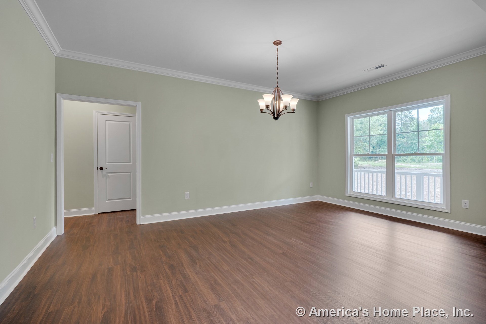 Dining room with wood-look plank flooring, soft green walls, crown molding, large double window with white trim and baseboards, central chandelier, and paneled interior door.