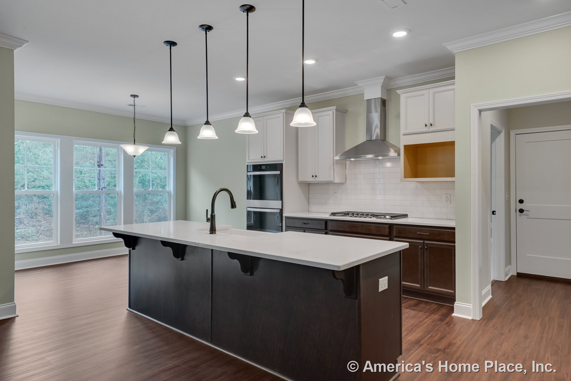 Spacious kitchen with large quartz island, white upper cabinets, dark lower cabinetry, subway tile backsplash, stainless steel range hood, double wall ovens, pendant and recessed