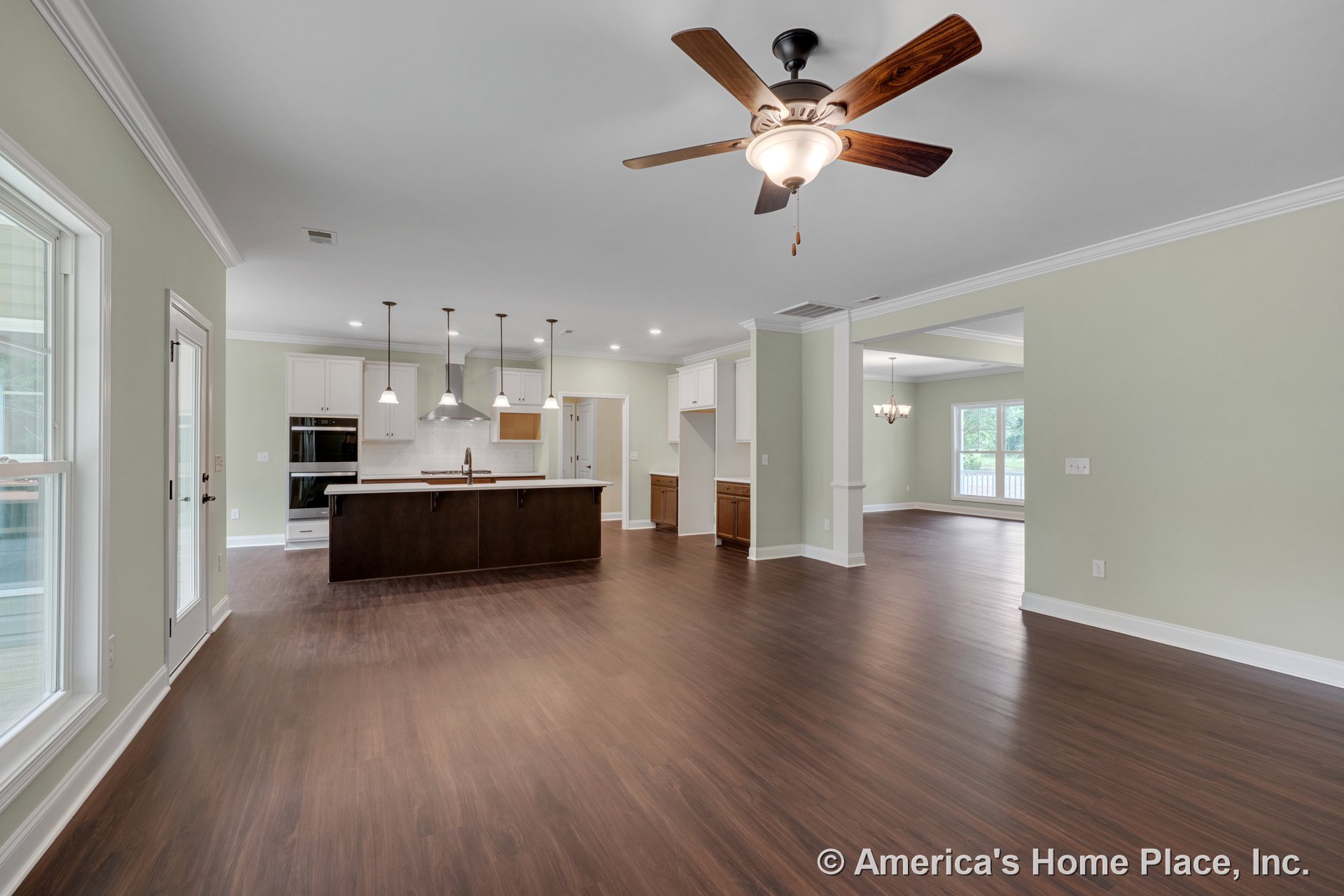 Open-concept kitchen and living area with dark wood island, white upper cabinets, pendant lights, ceiling fan with light, large windows, crown molding, double oven, recessed