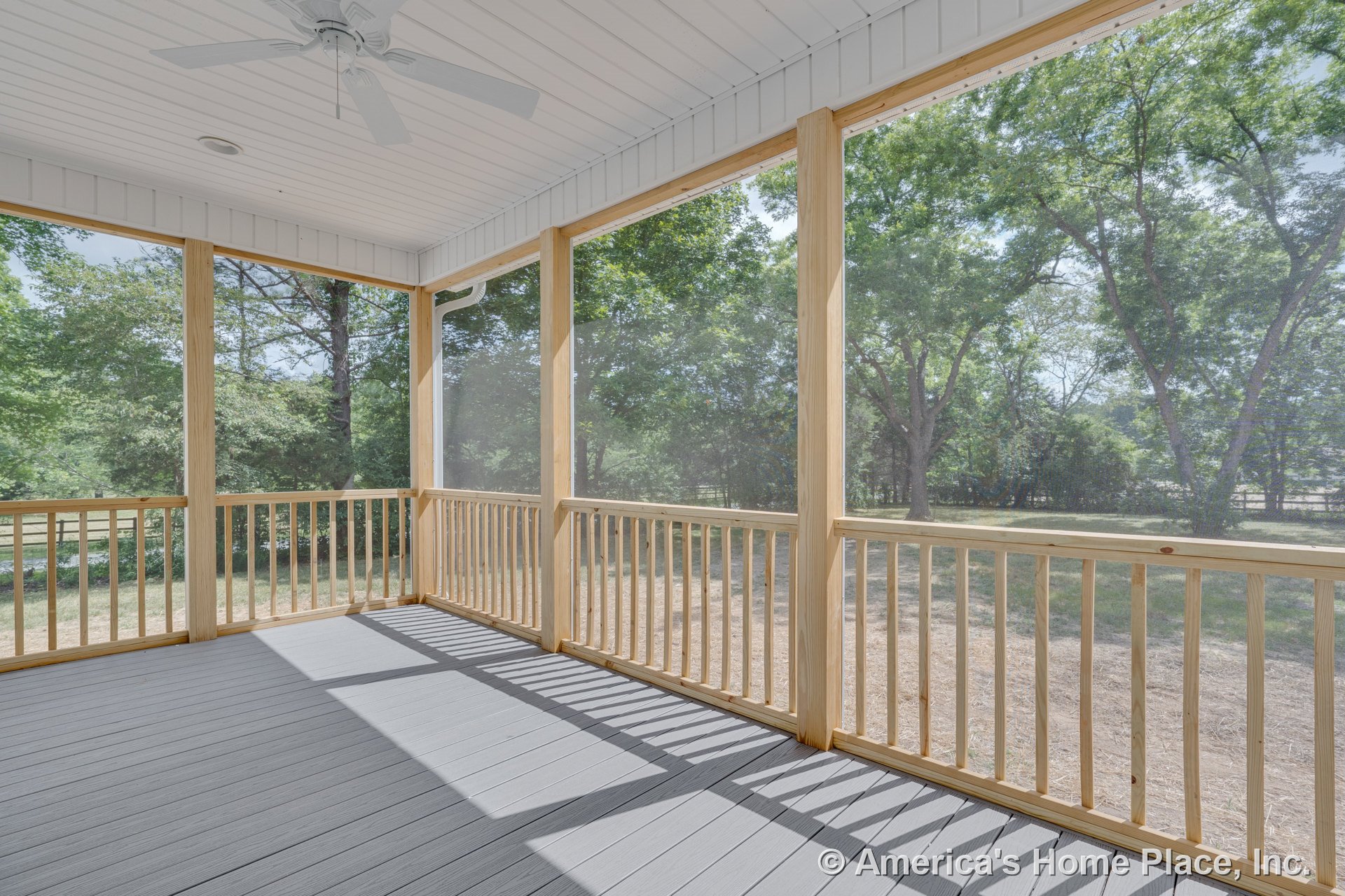 Screened porch with wood railings, composite deck flooring, white beadboard ceiling, and ceiling fan fixture, showcasing built-in outdoor living features and natural light.