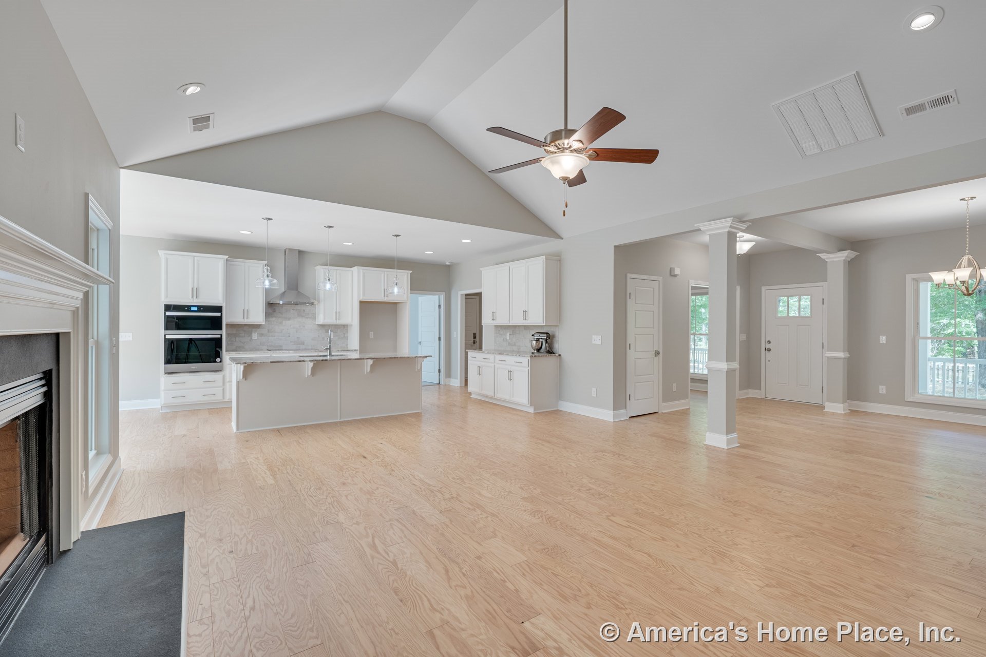 Open-concept living area with light wood floors, vaulted ceiling with recessed lighting, modern kitchen featuring white cabinetry, tile backsplash, kitchen island with pendant