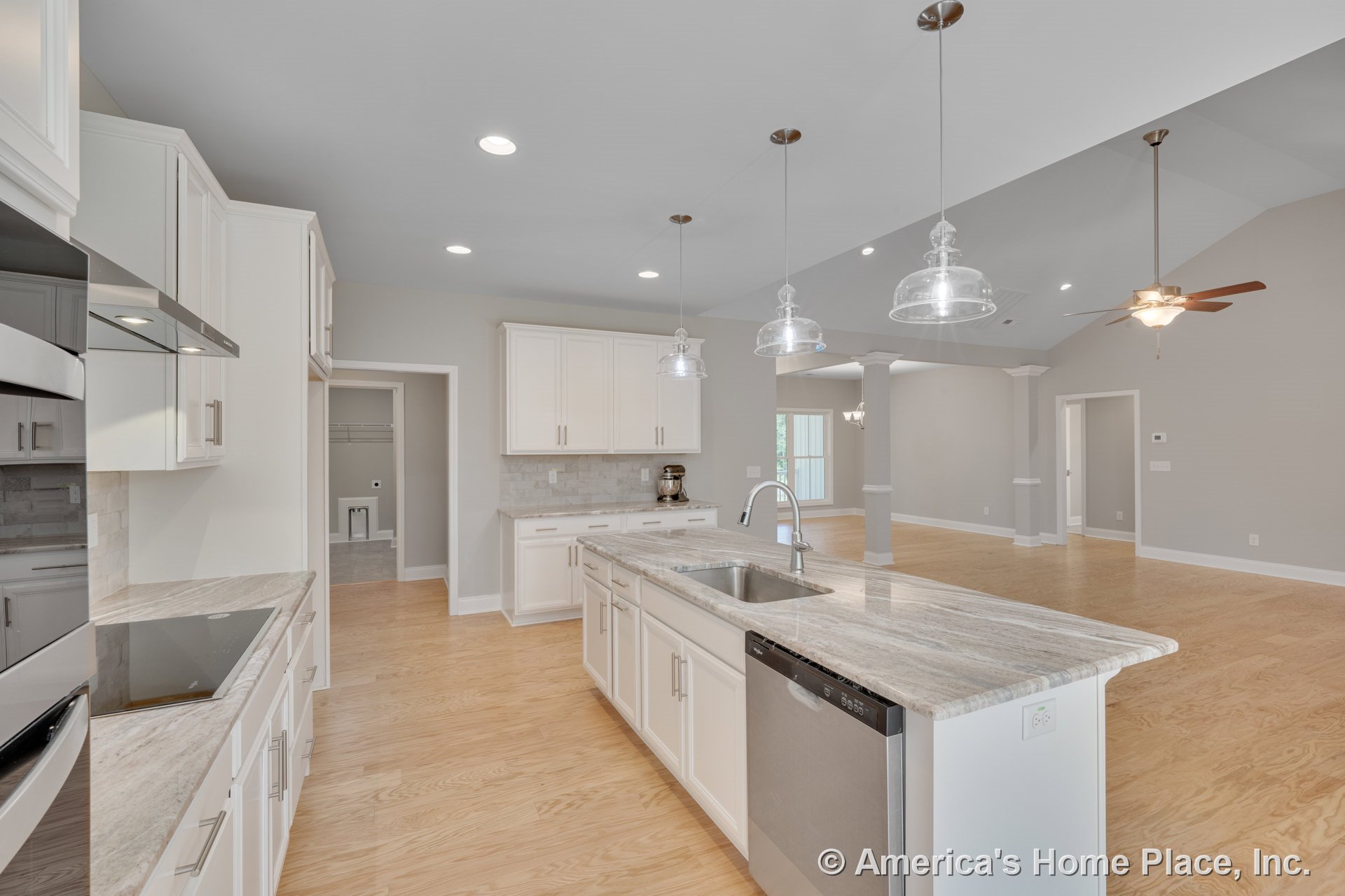 White shaker kitchen cabinets with stone island countertop, glass pendant lights, built-in appliances, tile backsplash, and column trim; open concept layout flows into spacious