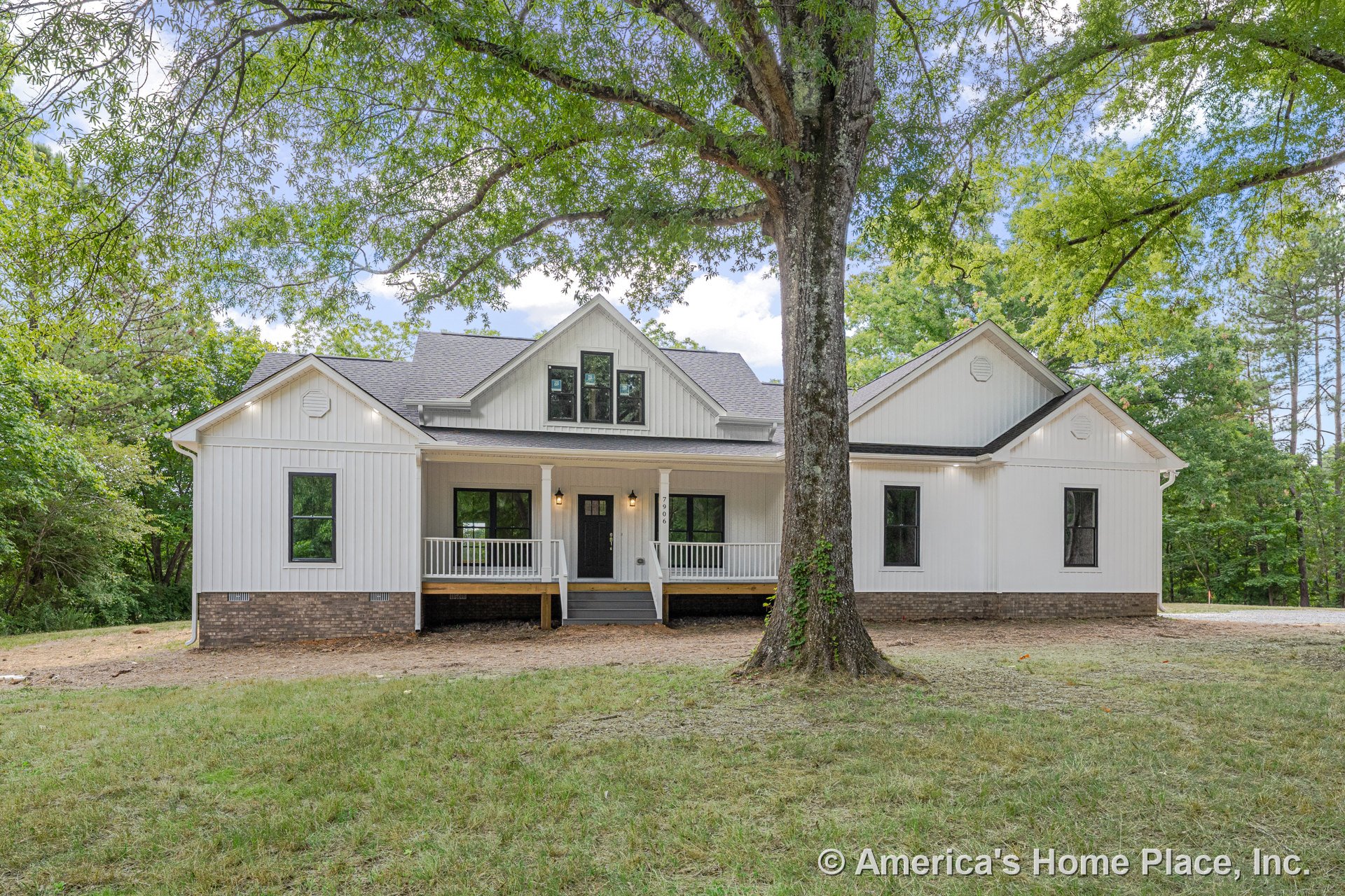 Covered front porch with white railings, board-and-batten siding, brick foundation, black framed windows, gable roof, and exterior lighting fixtures.