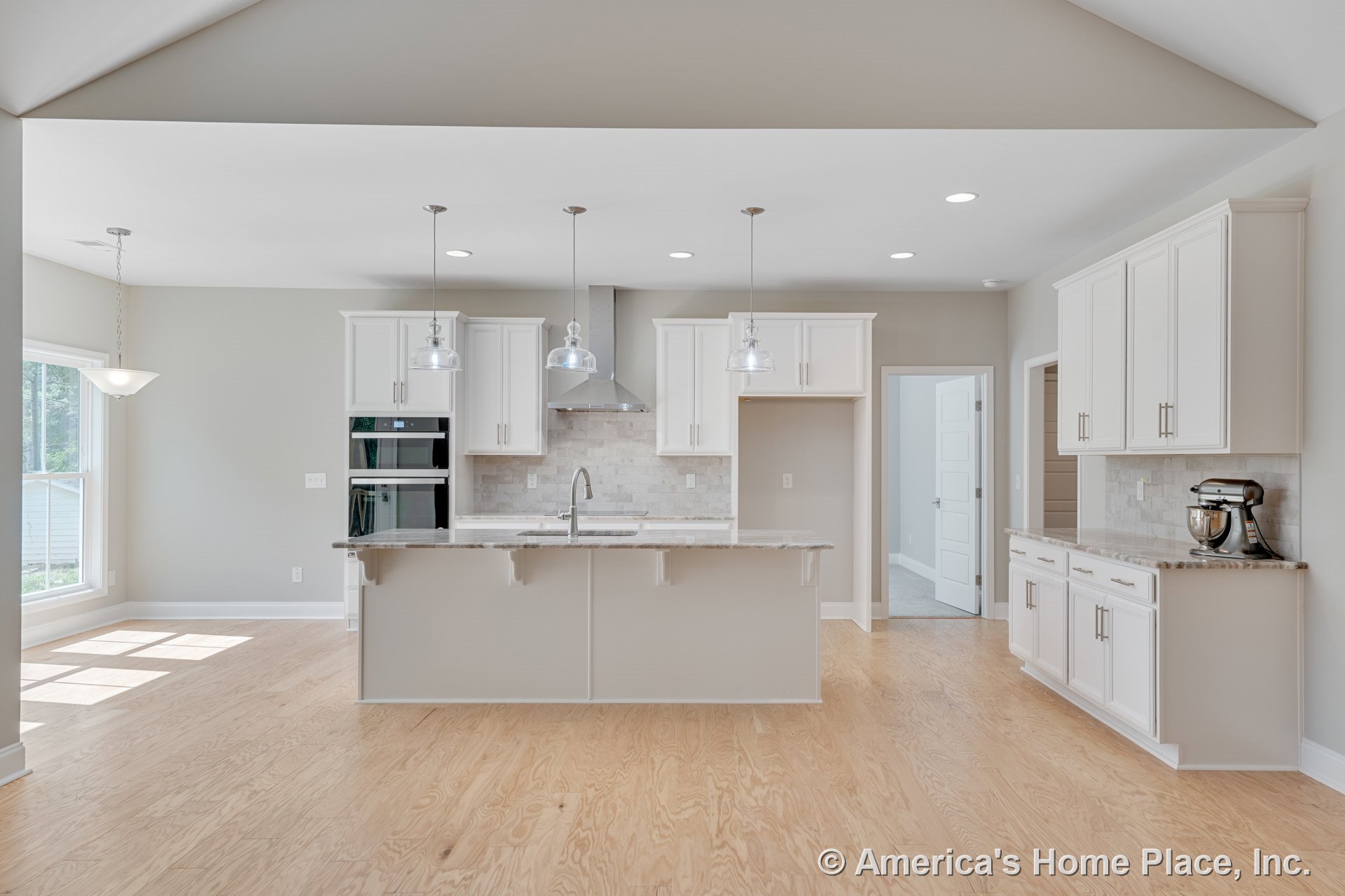 White shaker cabinets, central stone countertop island, tile backsplash, built-in double oven, pendant and recessed lighting, light wood flooring, range hood, windows, and open
