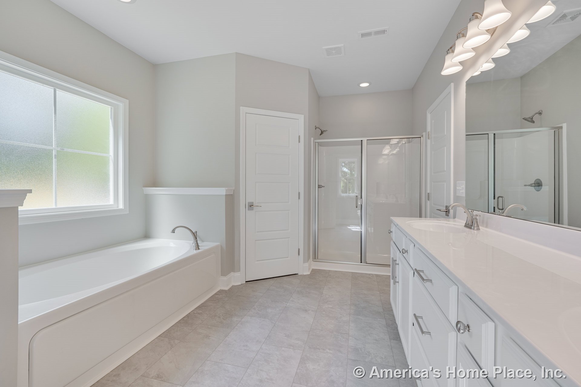 Large soaking tub beneath frosted window, glass-enclosed shower, double sink vanity with white shaker cabinets, chrome fixtures, wall-mounted lighting, neutral walls, and tile