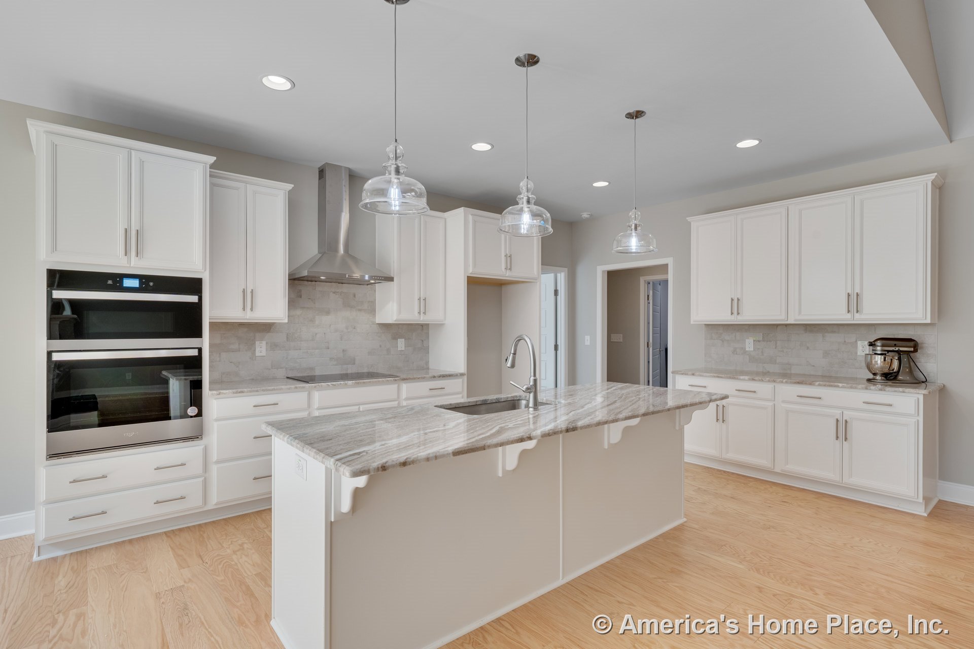 White shaker cabinets, marble kitchen island with waterfall edge, stainless steel range hood and double wall oven, glass pendant lights, light wood flooring, tile backsplash