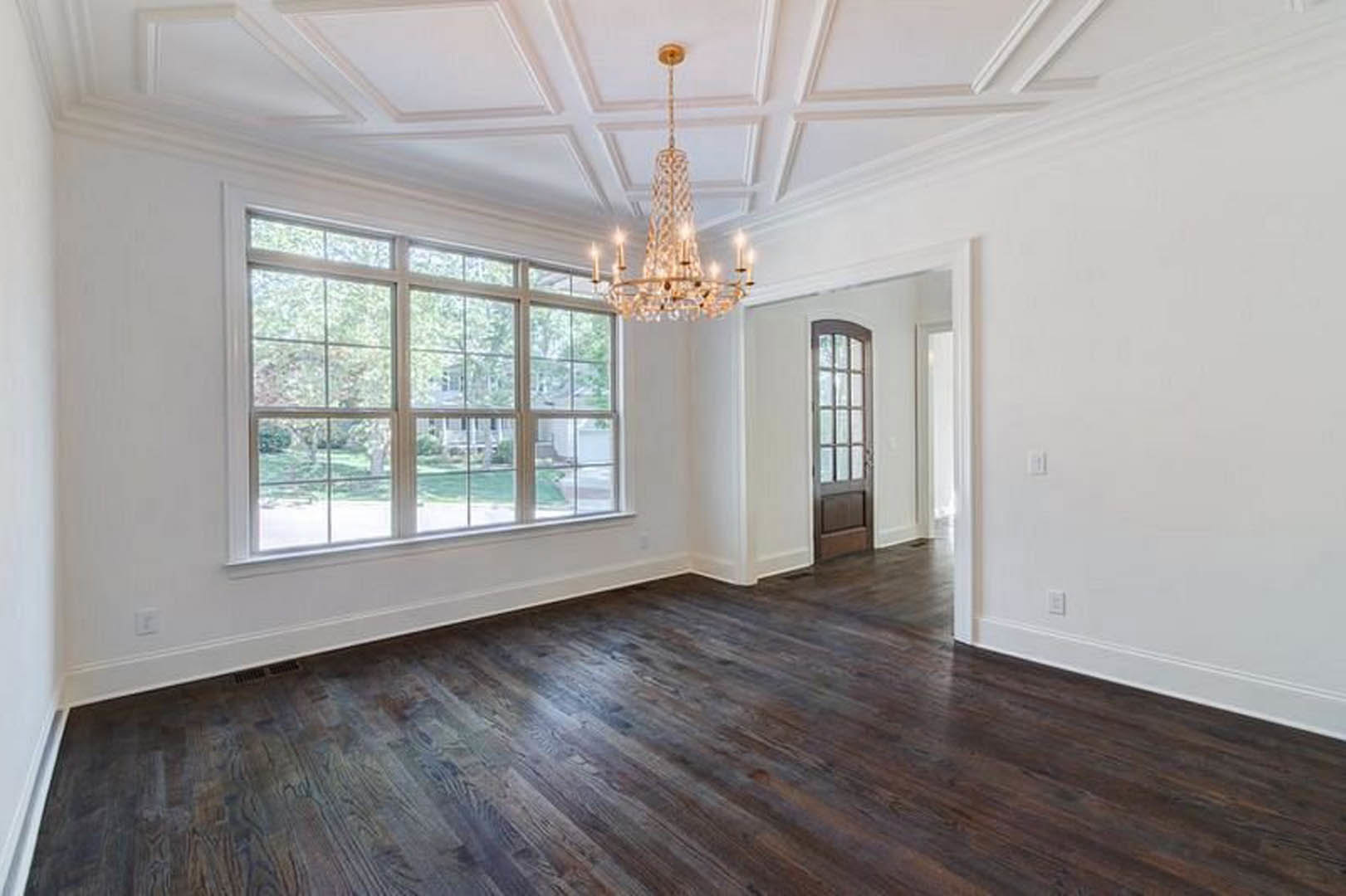 Chandelier hanging from ceiling above dark wood flooring, large multi-pane windows along wall, white molding and plaster finishes