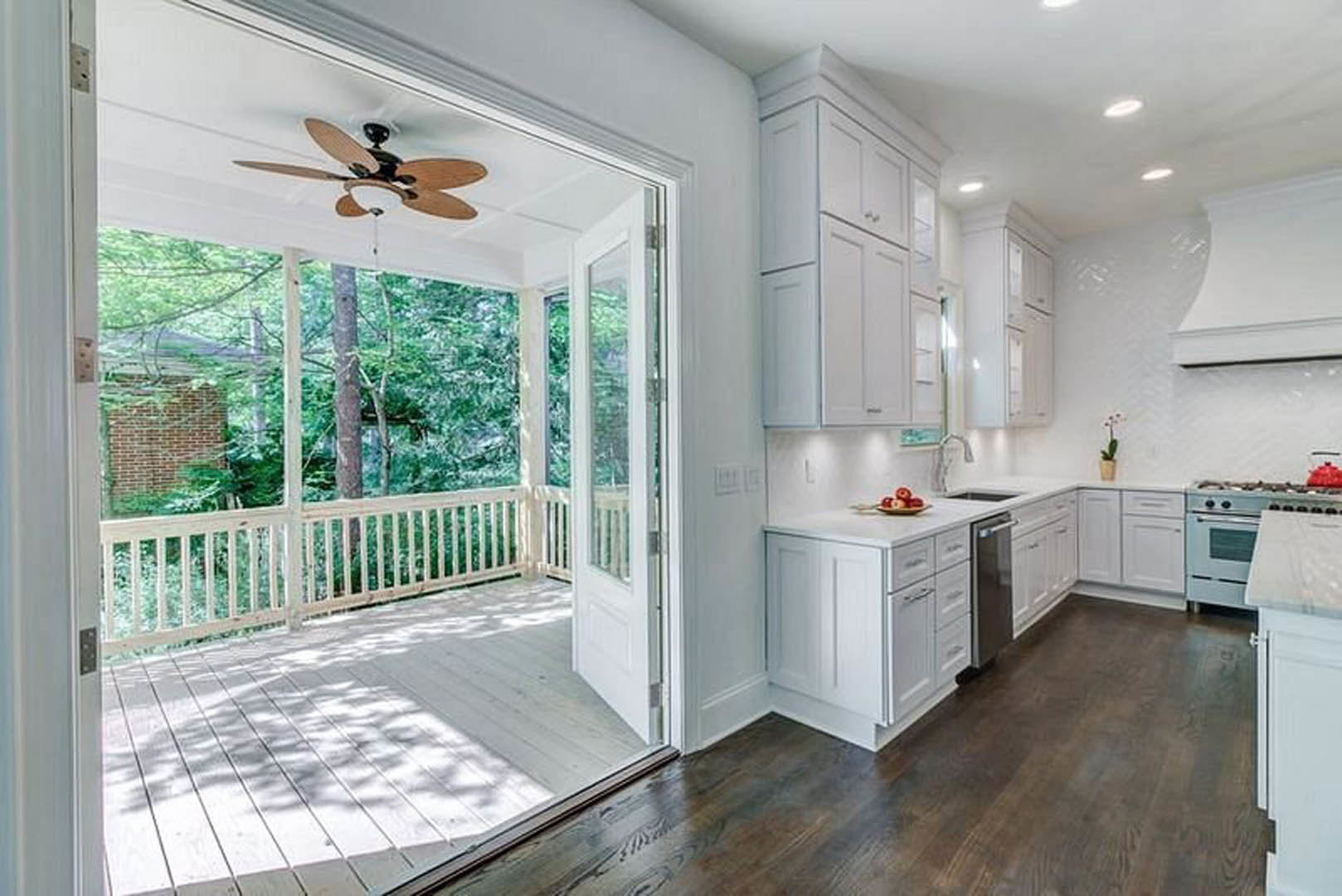 Open kitchen with light cabinetry, stainless appliances, and a central island, adjacent to a white deck with railing and balcony, ceiling fan overhead, sunlight casting tree