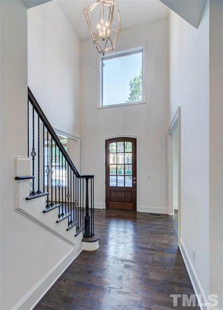 Hardwood floor entry with black metal staircase railing, white walls, paneled door, and modern light fixture near window