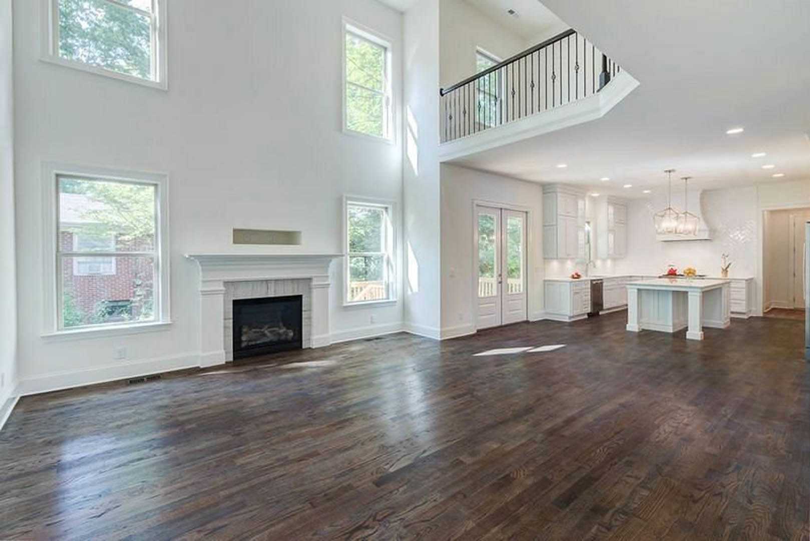 Spacious white living area with hardwood floors, modern fireplace with black glass door, white staircase with metal railing, large window overlooking brick building