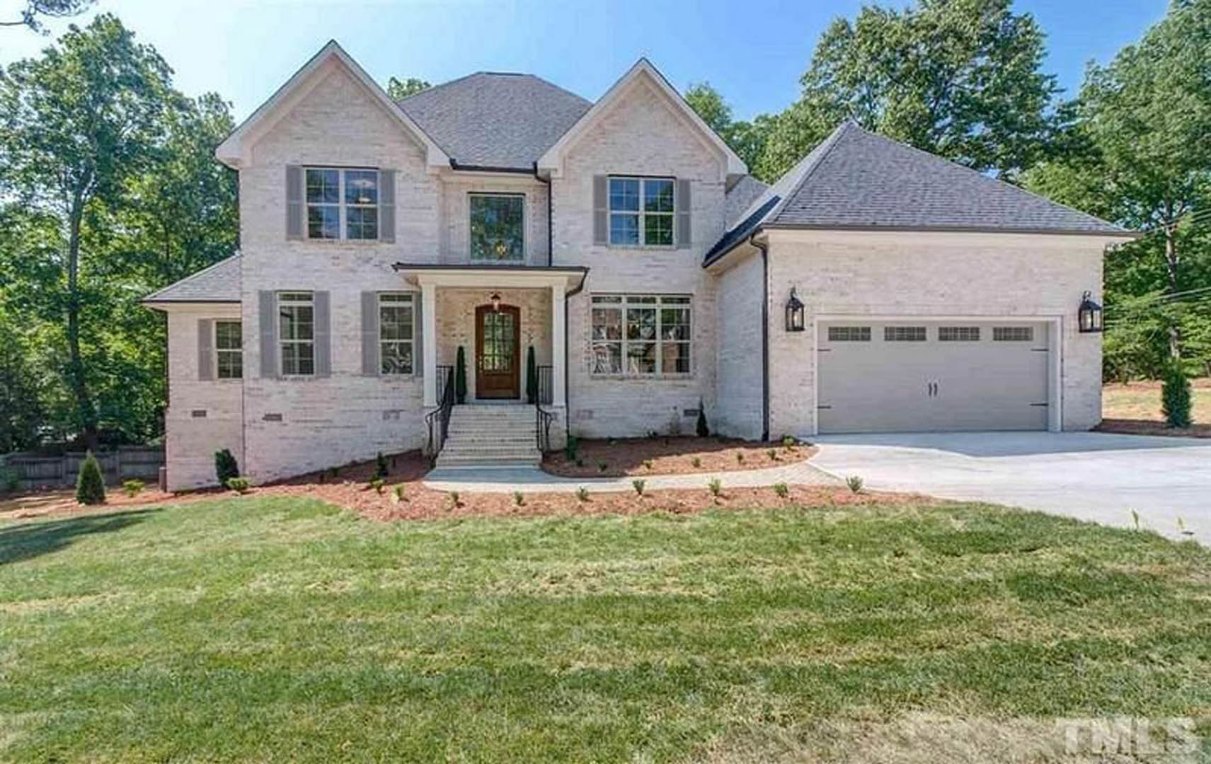 Two-story house with white siding, large windows, covered front porch, green lawn, paved driveway, and mature trees in the yard