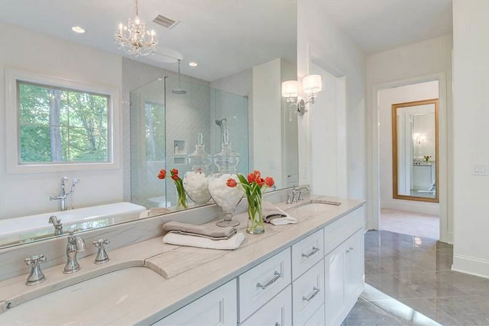 Bathroom featuring a wide framed mirror above a stone countertop, freestanding soaking tub, tiled walls, and a window overlooking leafy trees