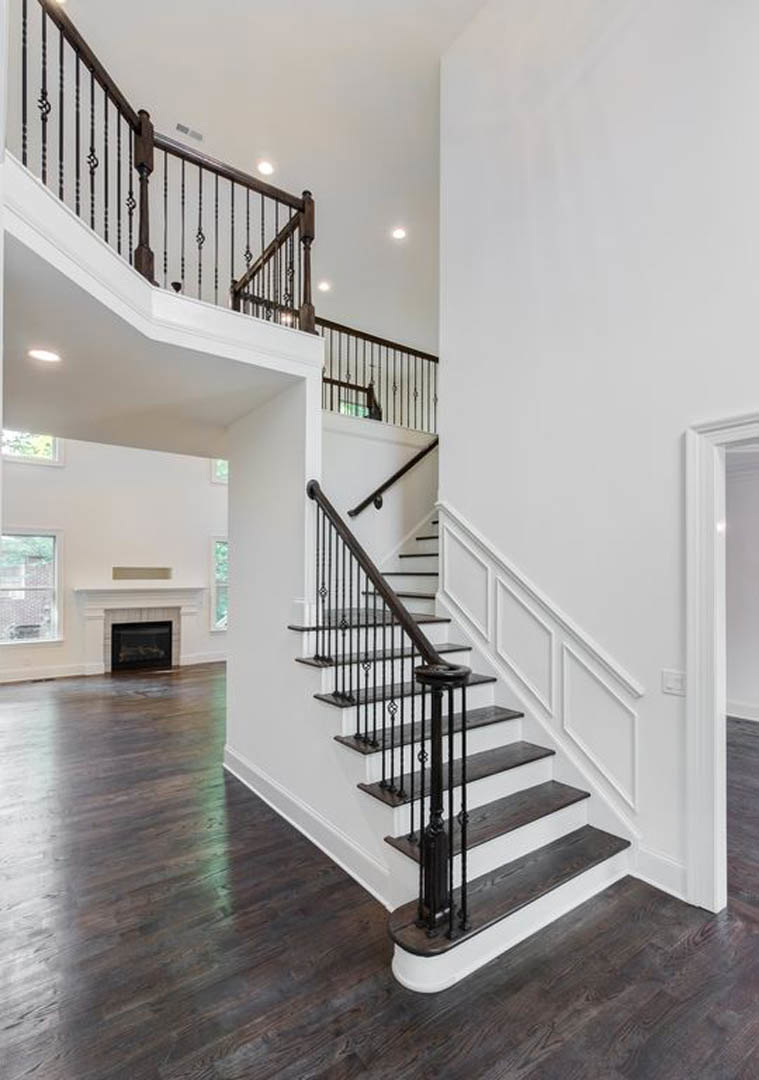 Wood staircase with black metal railings, laminate flooring, white walls, and partial view of modern fireplace in open living area