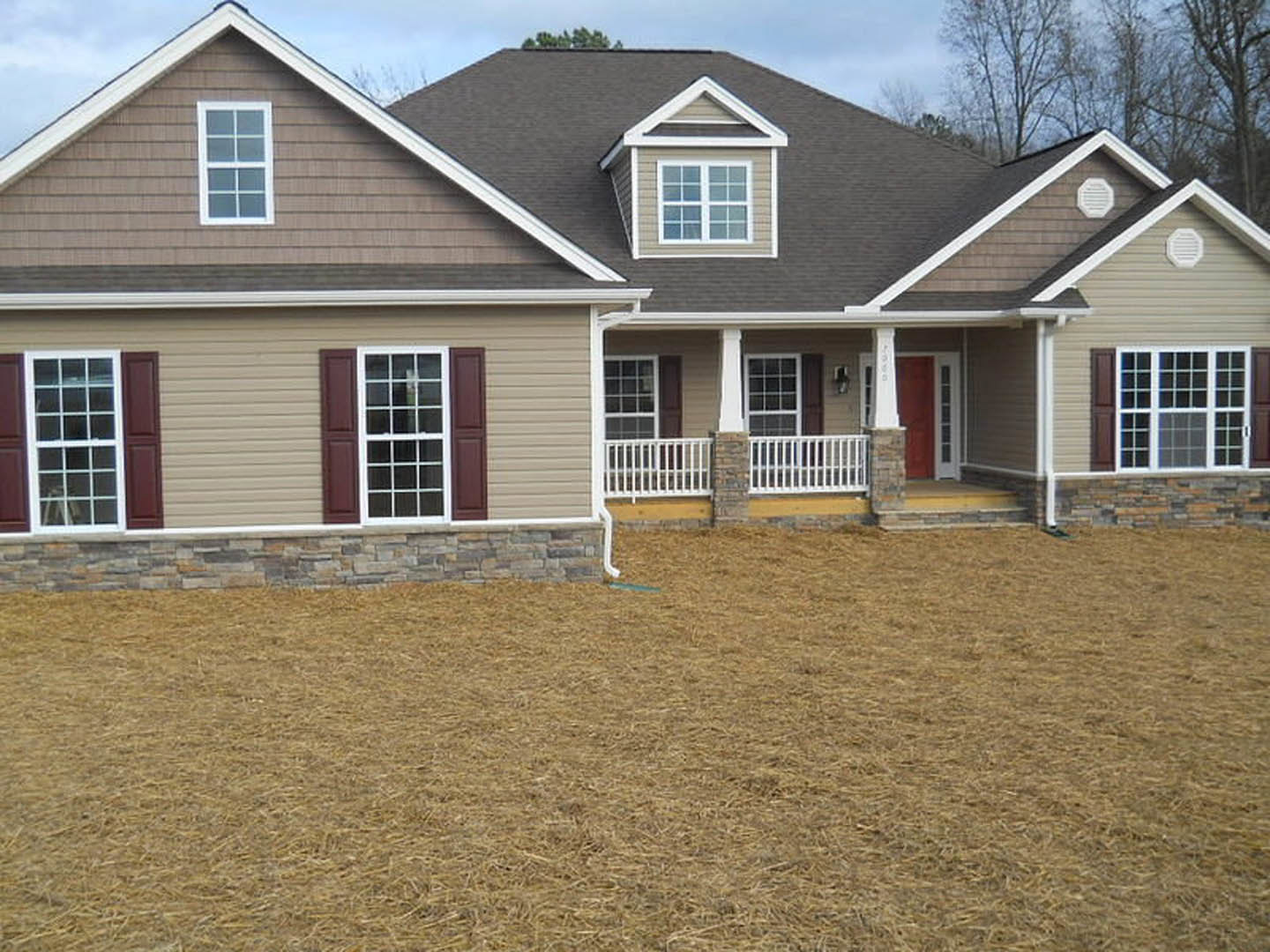 Brick house with white gutters, white-framed windows, white metal bar and vent on exterior wall, covered porch, and grassy yard under blue sky
