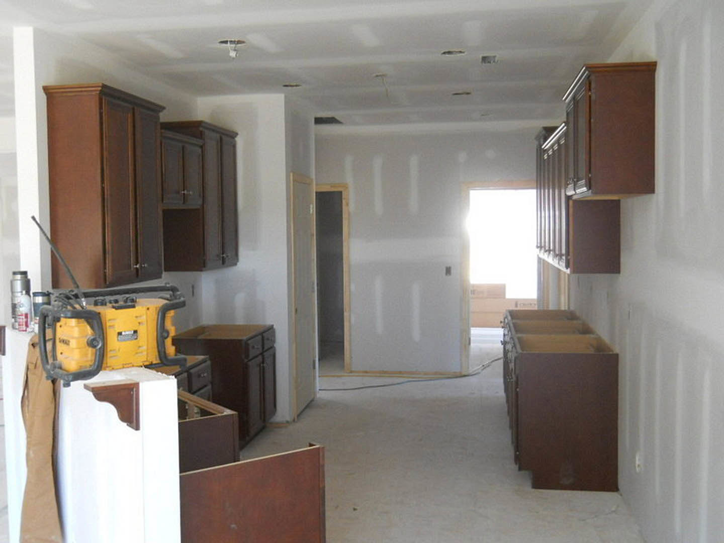 Kitchen featuring wood cabinetry, light-colored countertops, and a white wall, with natural light streaming through a nearby door.