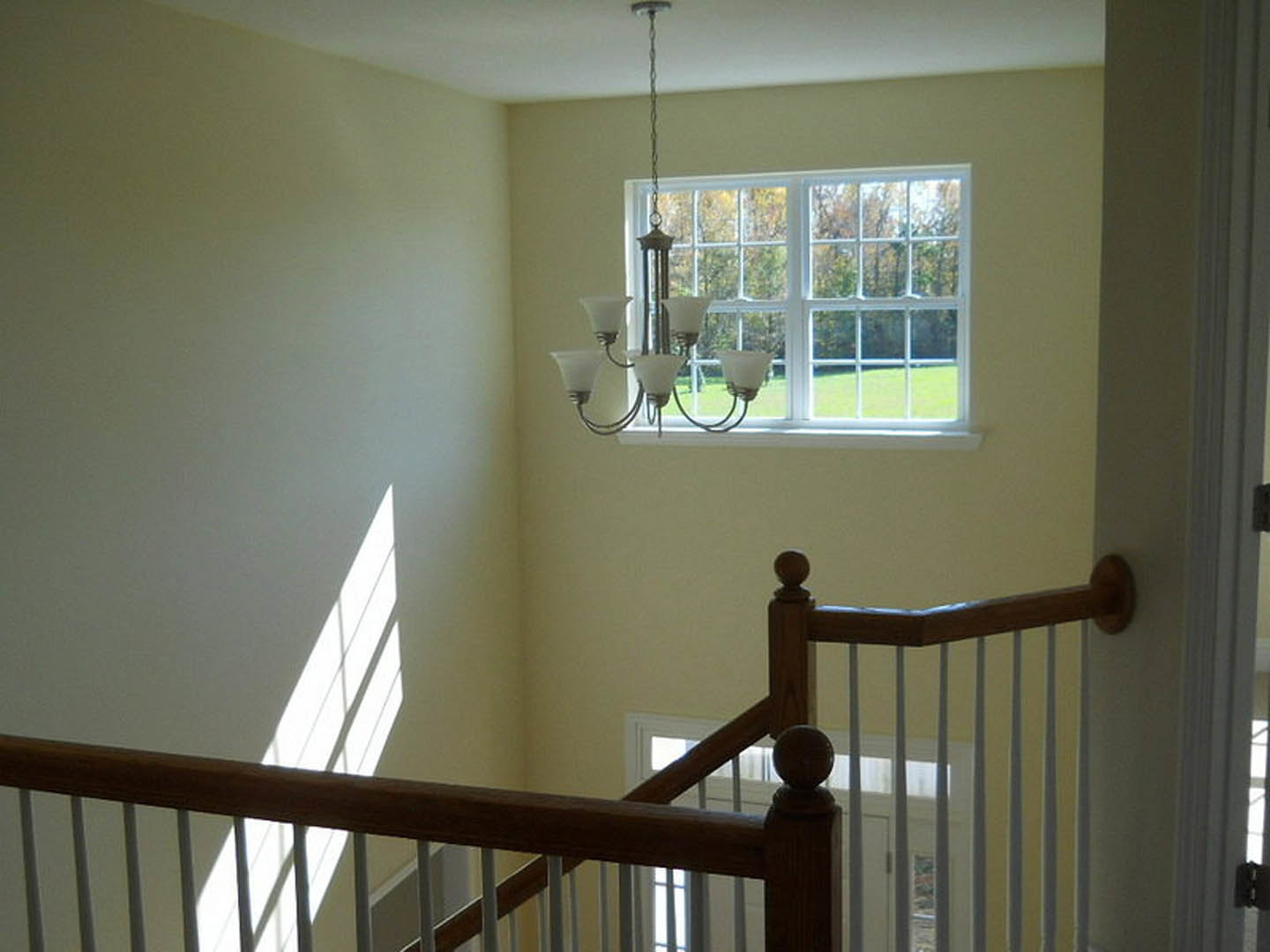 Chandelier with glass globes hanging from ceiling near large window with white frame, wooden staircase railing, and decorative molding on walls
