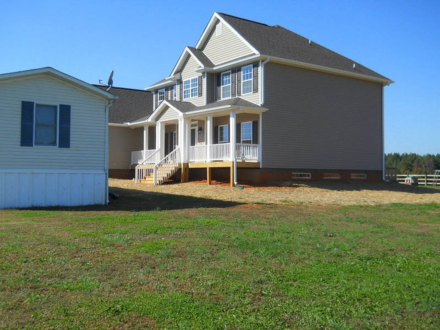 Two-story home with light siding, blue shuttered windows, covered front porch, white railing, manicured lawn, and clear sky