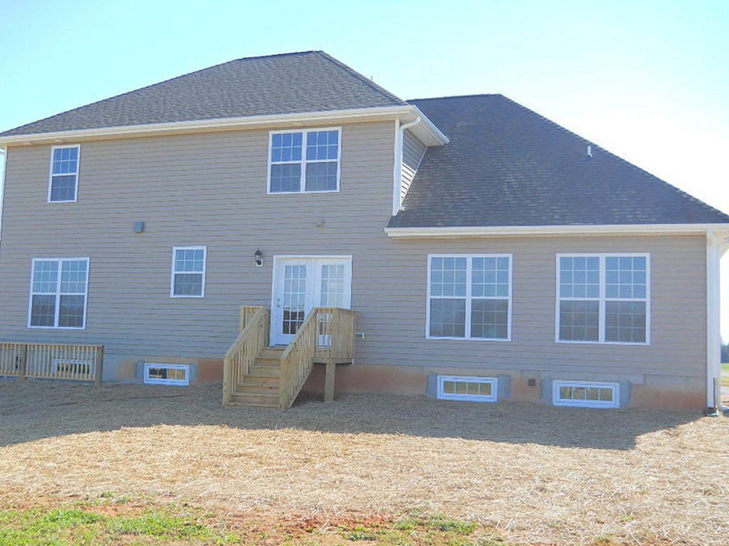 Two-story home with light siding, wooden exterior staircase, white door with glass panes, and multiple windows; blue sky and grassy yard in foreground