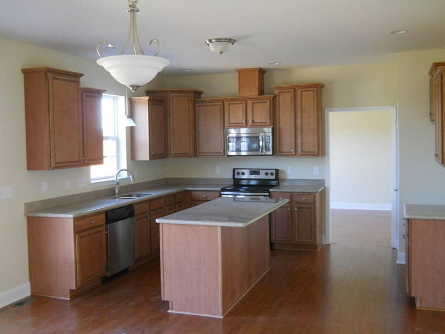 Kitchen with natural wood cabinets, marble-topped island, stainless steel microwave, modern light fixture, white ceiling, and white wall with matching door