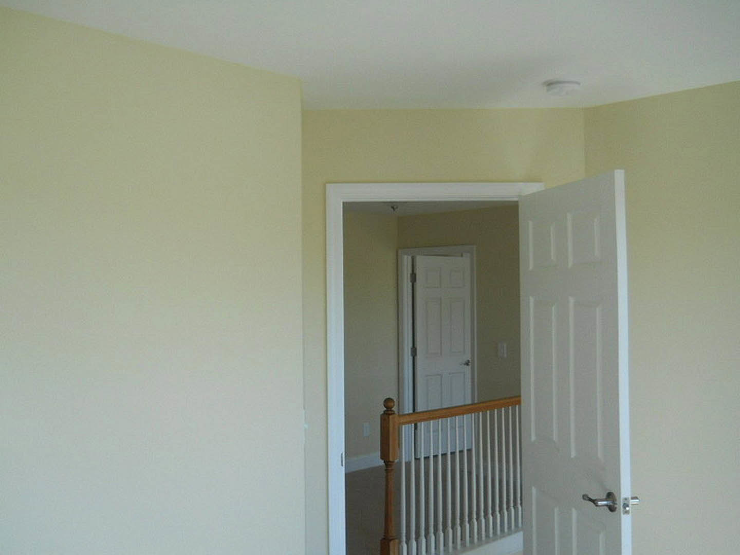 White door with silver handle open to reveal wooden staircase and railing, plaster walls, and ceiling molding in a residential interior.