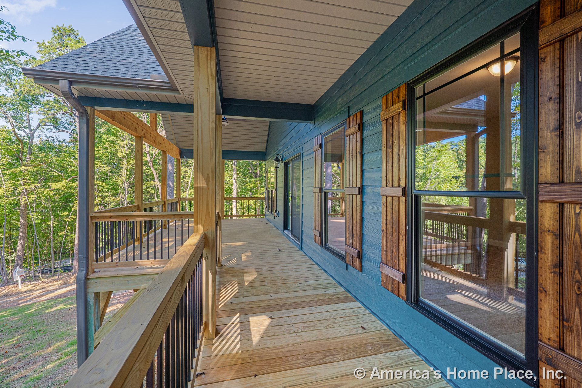 Spacious covered porch with wood plank flooring, large windows framed by rustic wood shutters, wood railing with metal balusters, exterior blue siding, outdoor ceiling light