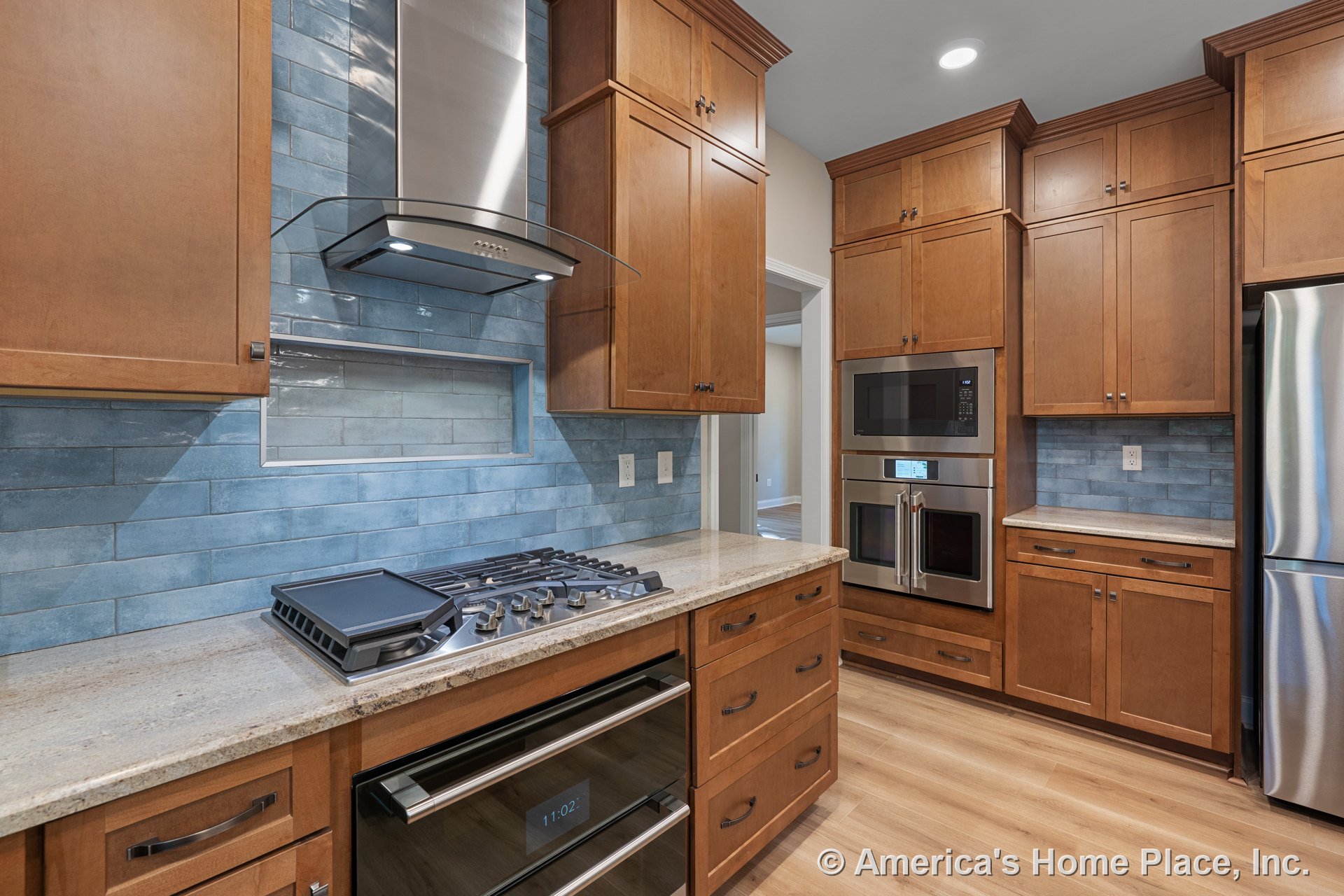 Wood cabinetry kitchen with blue subway tile backsplash, stainless steel range hood, built-in microwave and oven, granite countertops, light wood flooring, recessed lighting, and