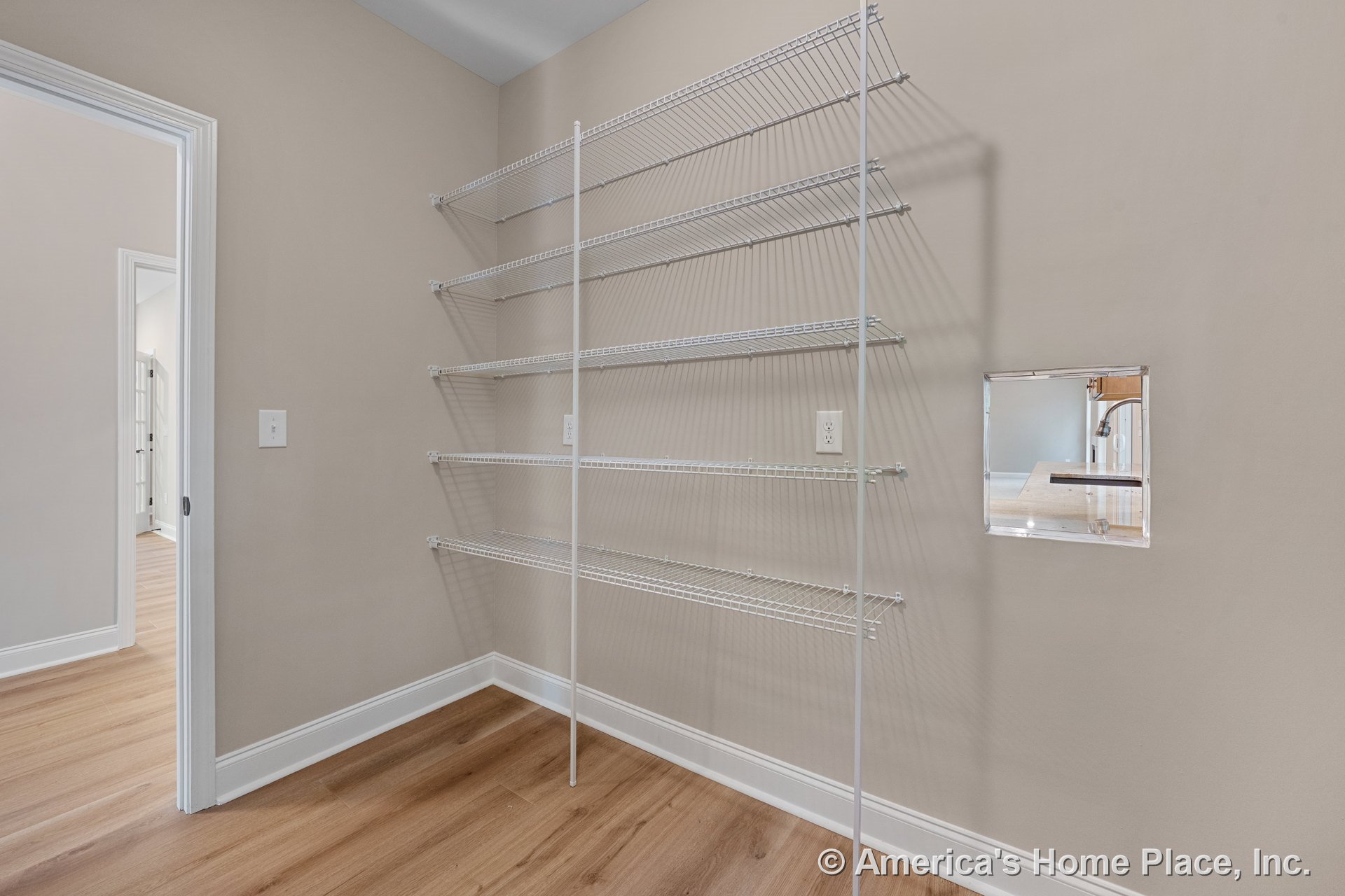 Pantry with built-in white wire shelving, light wood flooring, beige painted walls, baseboard trim, wall outlet, and utility access panel near doorway.
