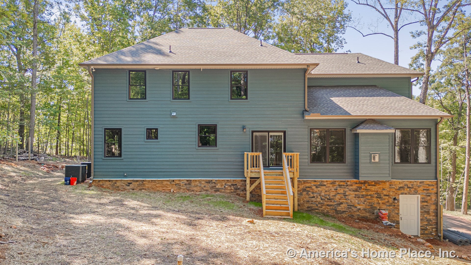 Blue horizontal lap siding with stone veneer foundation, black-framed windows, wooden entry stairs leading to covered porch, gabled roof, exterior utility door, built-in lighting