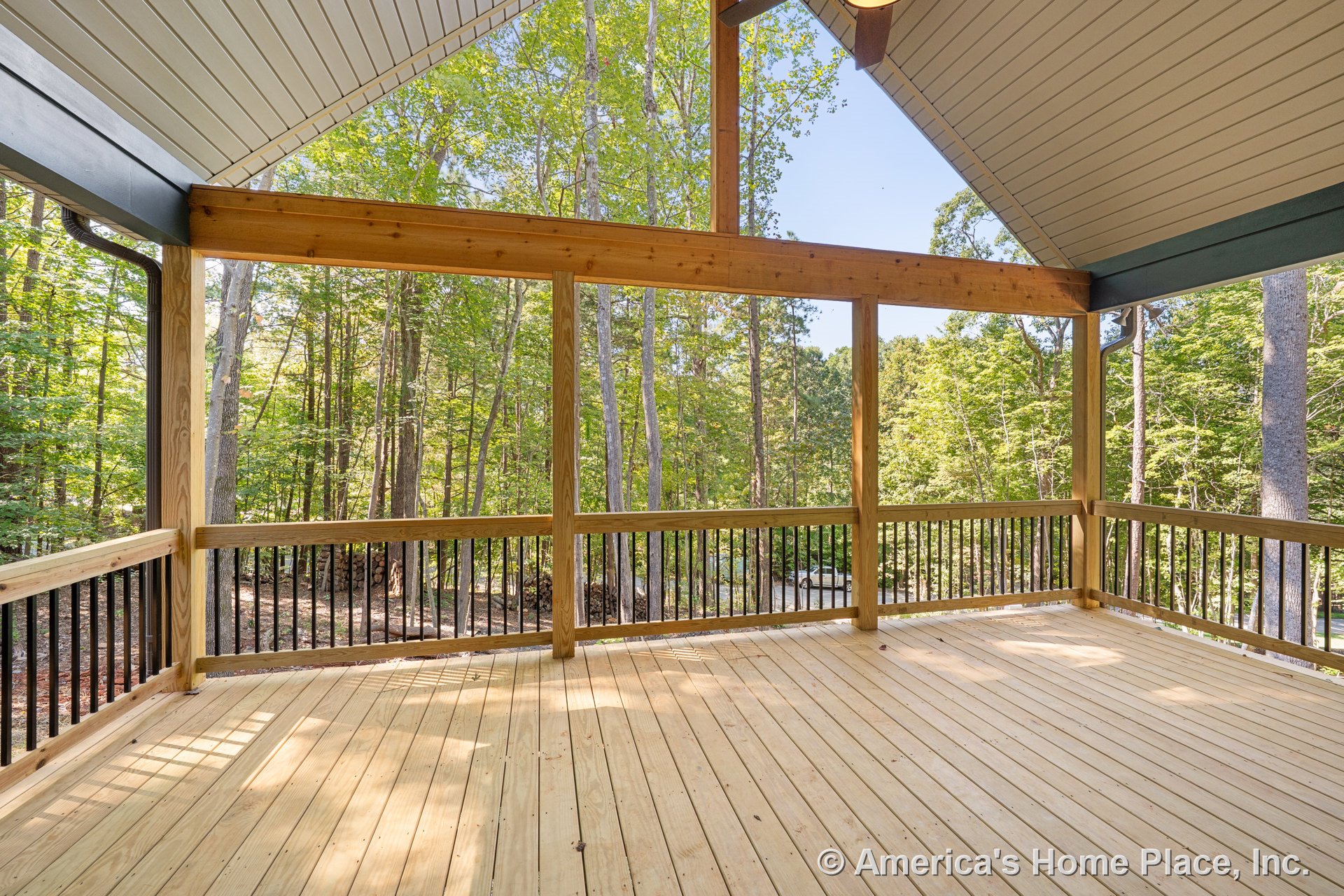 Covered porch with vaulted ceiling and exposed wood beams, wood plank flooring, open wood railing with black balusters, trimmed roof edges, and large openings providing natural
