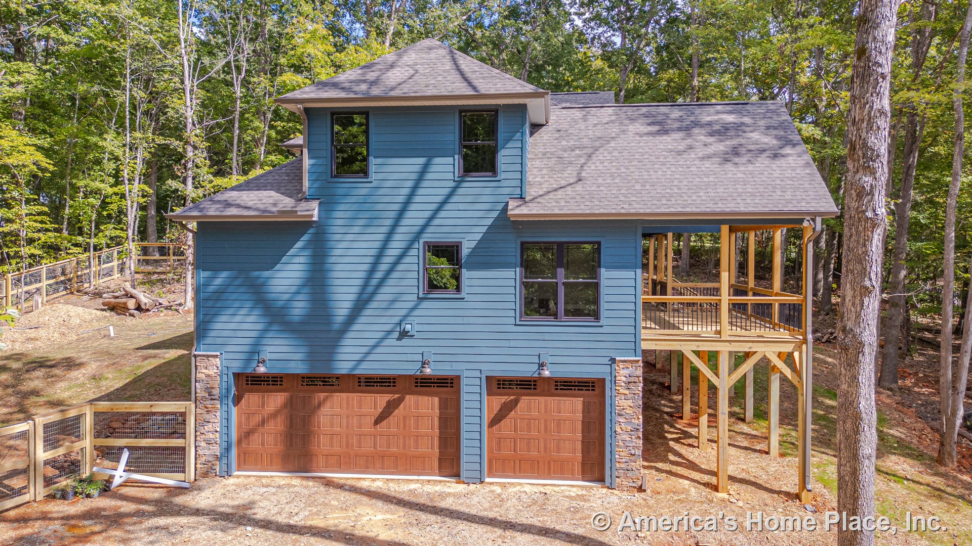Blue horizontal siding with stone veneer trim, gabled roof, covered elevated porch supported by wood posts, black framed windows, three-car garage with wooden doors, outdoor