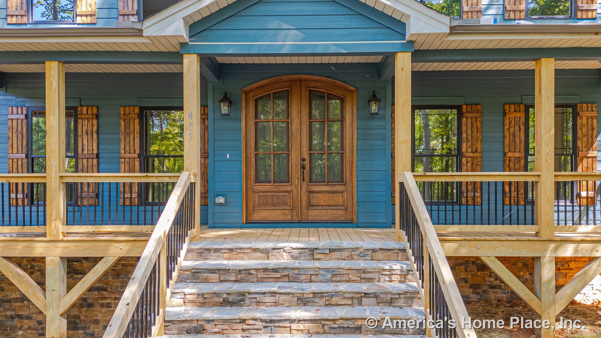 Covered front porch with stone steps, wood railings, double wooden entry doors, blue siding, wood window shutters, black metal railings, permanent lighting, and decorative trim.