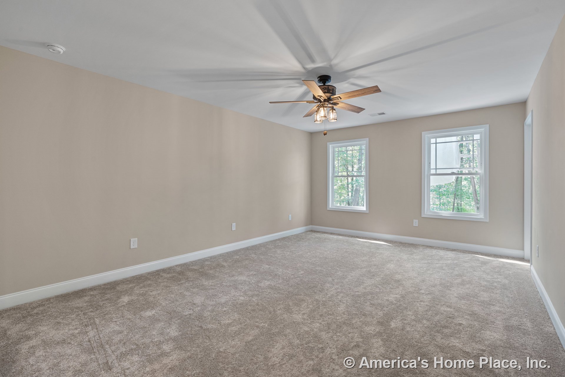 Spacious bedroom with beige carpet flooring, two large windows allowing natural light, neutral wall color, white baseboard trim, ceiling fan with integrated lighting, and smoke