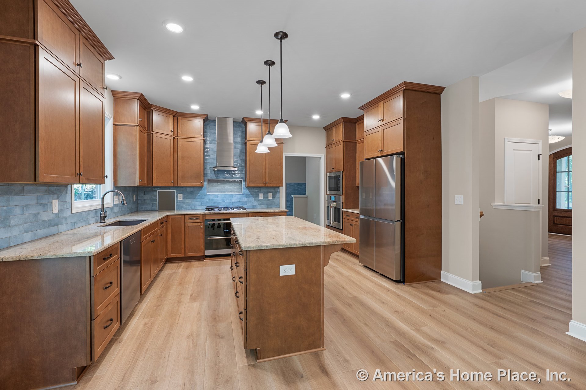 Custom kitchen with wood cabinetry, central island topped with granite, blue tile backsplash, stainless steel refrigerator, double oven, range hood, dishwasher, pendant and