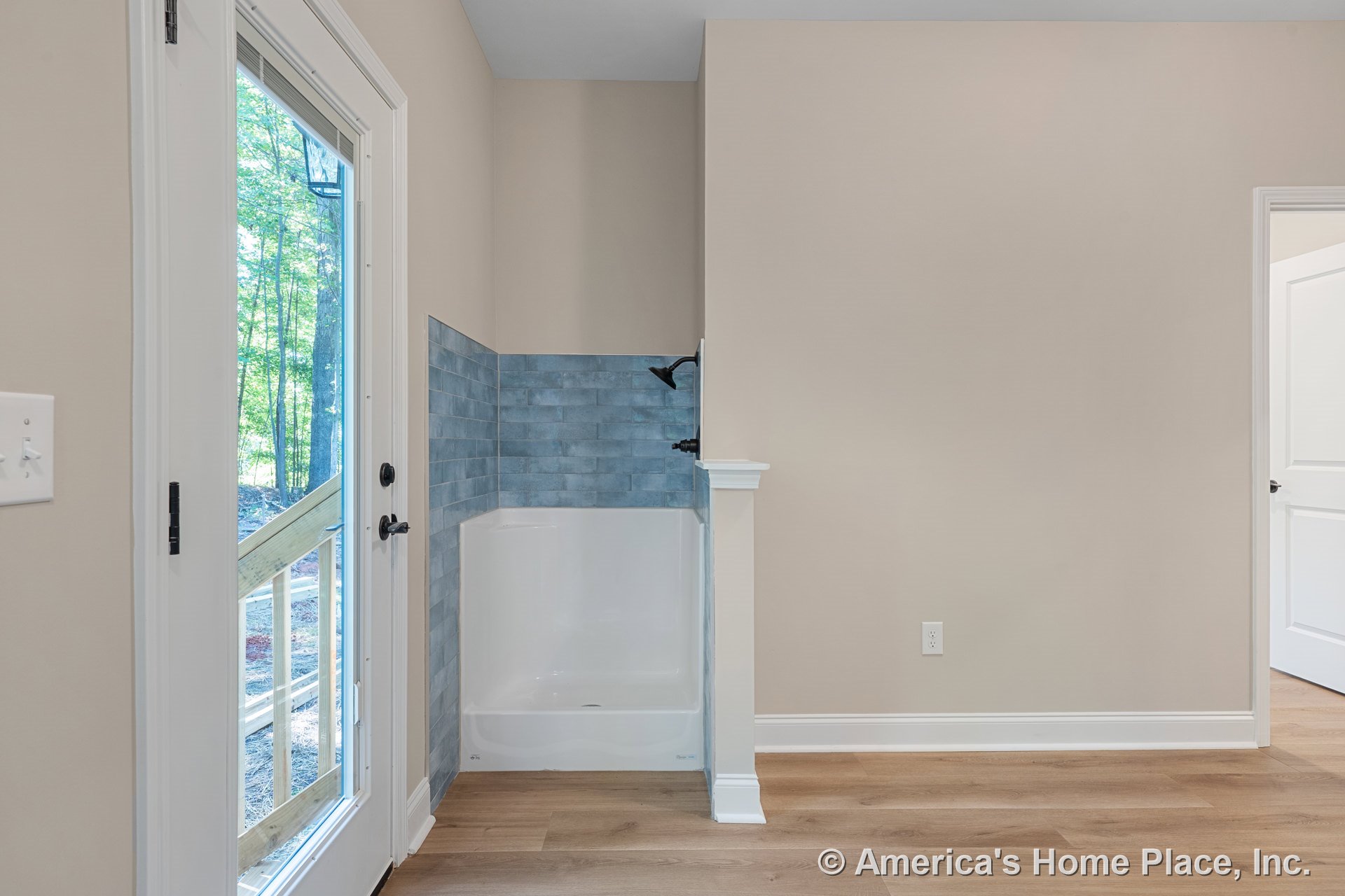 Mudroom with built-in shower featuring blue tile surround, glass exterior door, wood-look flooring, white trim and baseboards, beige painted walls, and black shower fixtures.