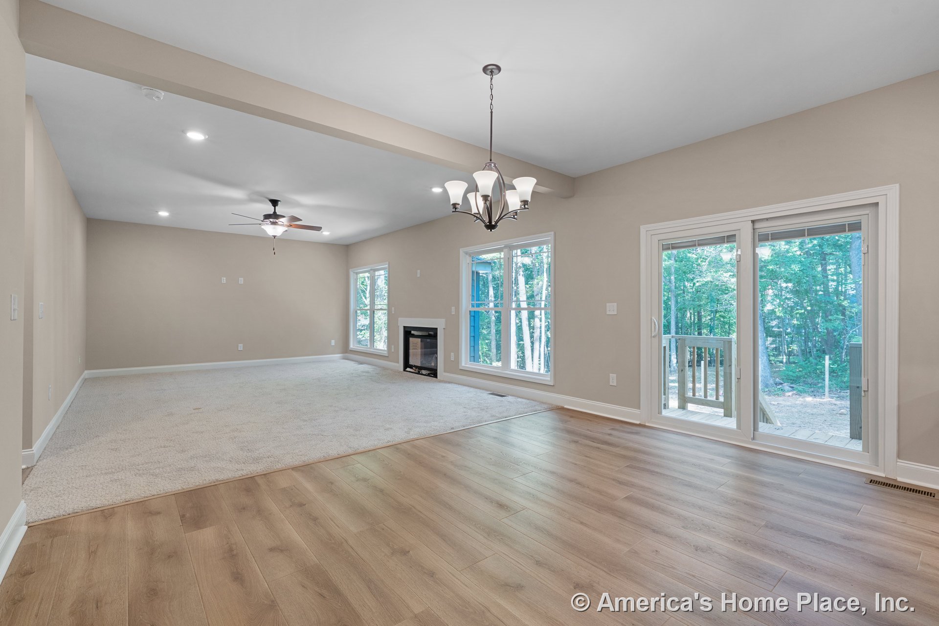 Open concept living and dining area with large double windows, sliding glass patio door, ceiling fan with light, chandelier above dining space, built-in fireplace, carpet and wood