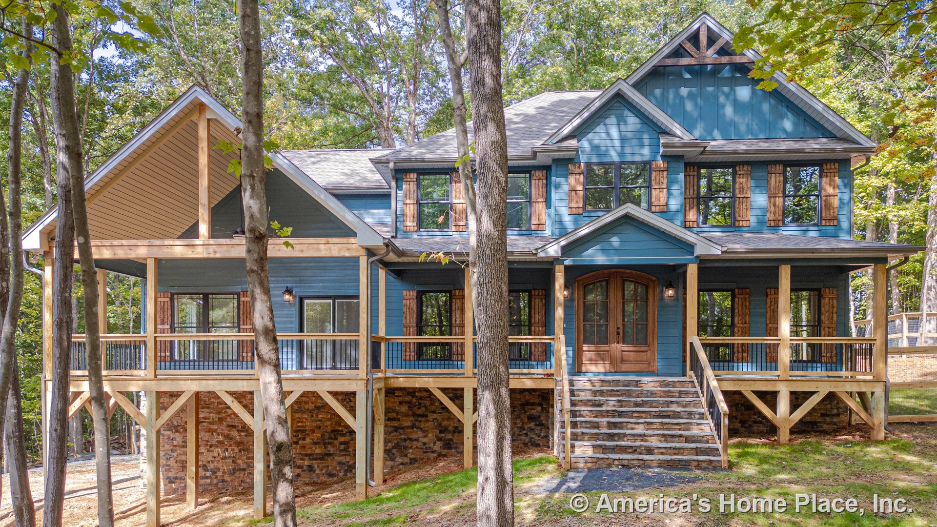 Large covered front porch with wood railings and stone steps, blue siding exterior with wood trim and shutters, multiple large windows, stone foundation, gable roof design, and