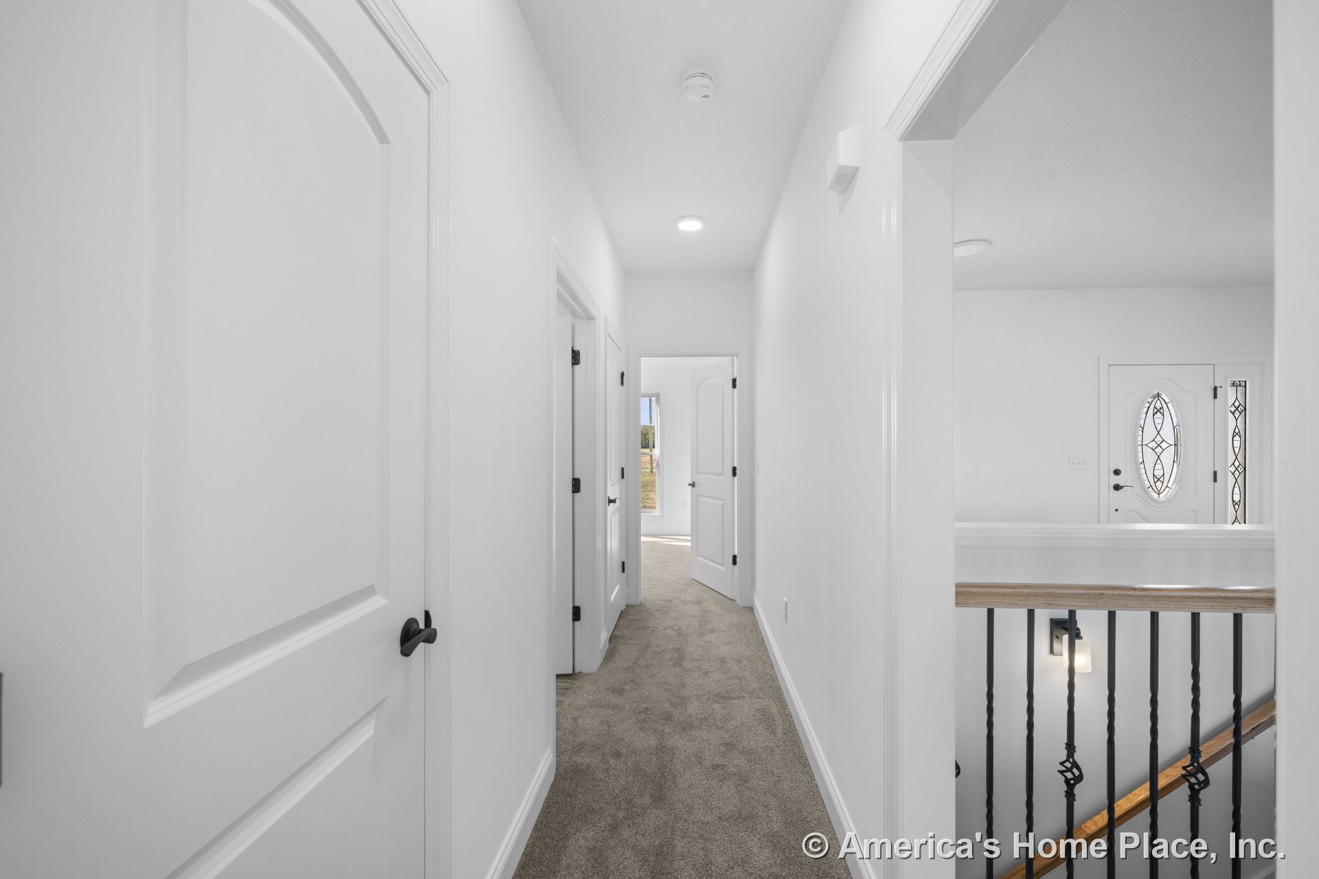 Hallway with white paneled doors, carpet flooring, black metal stair railing, white trim and baseboards, recessed ceiling light, and decorative glass front door.