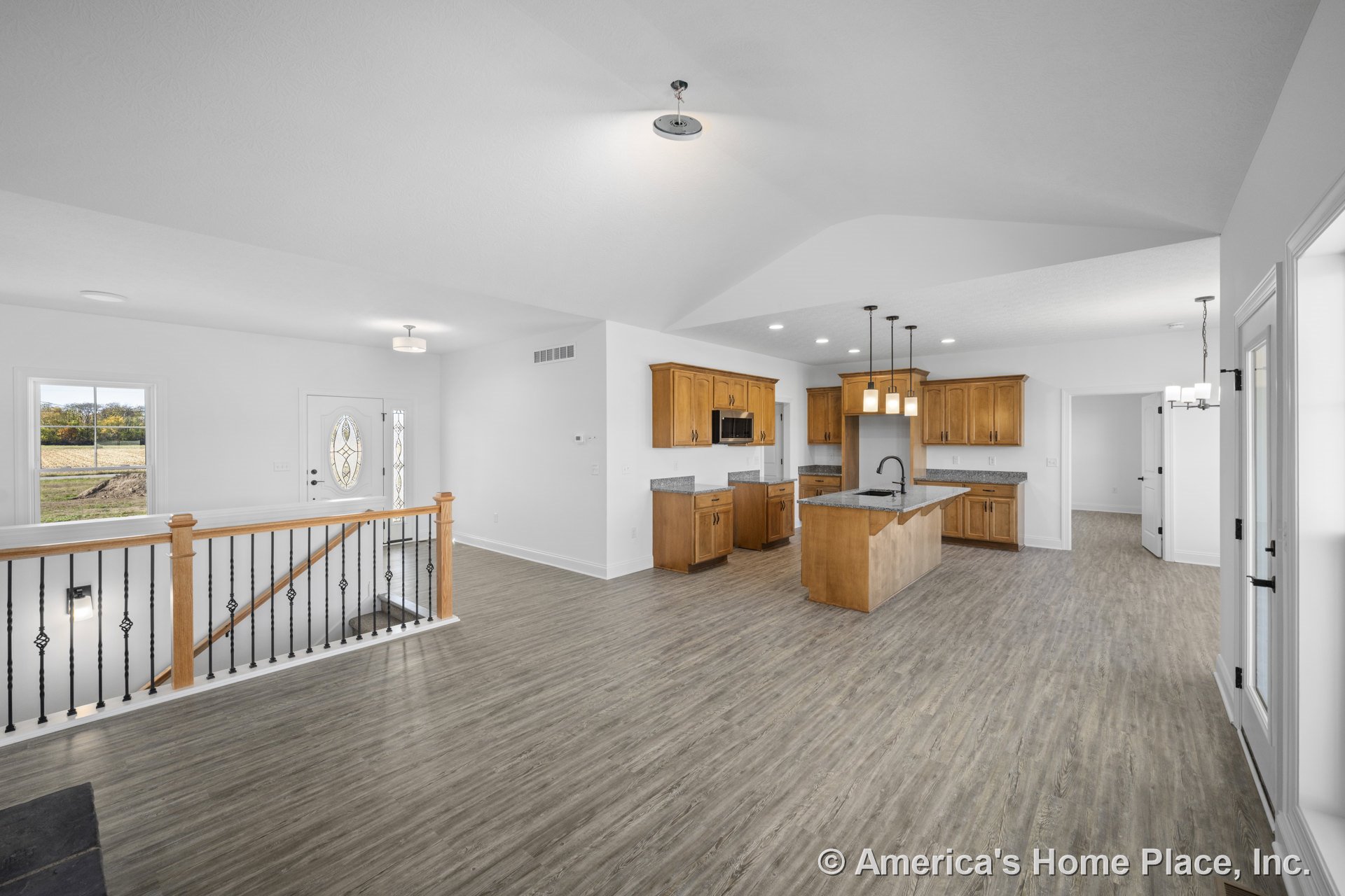Open kitchen with wood cabinetry, granite countertops, and pendant lights above the island, adjoining a spacious entry and living area with vinyl plank flooring, iron and wood