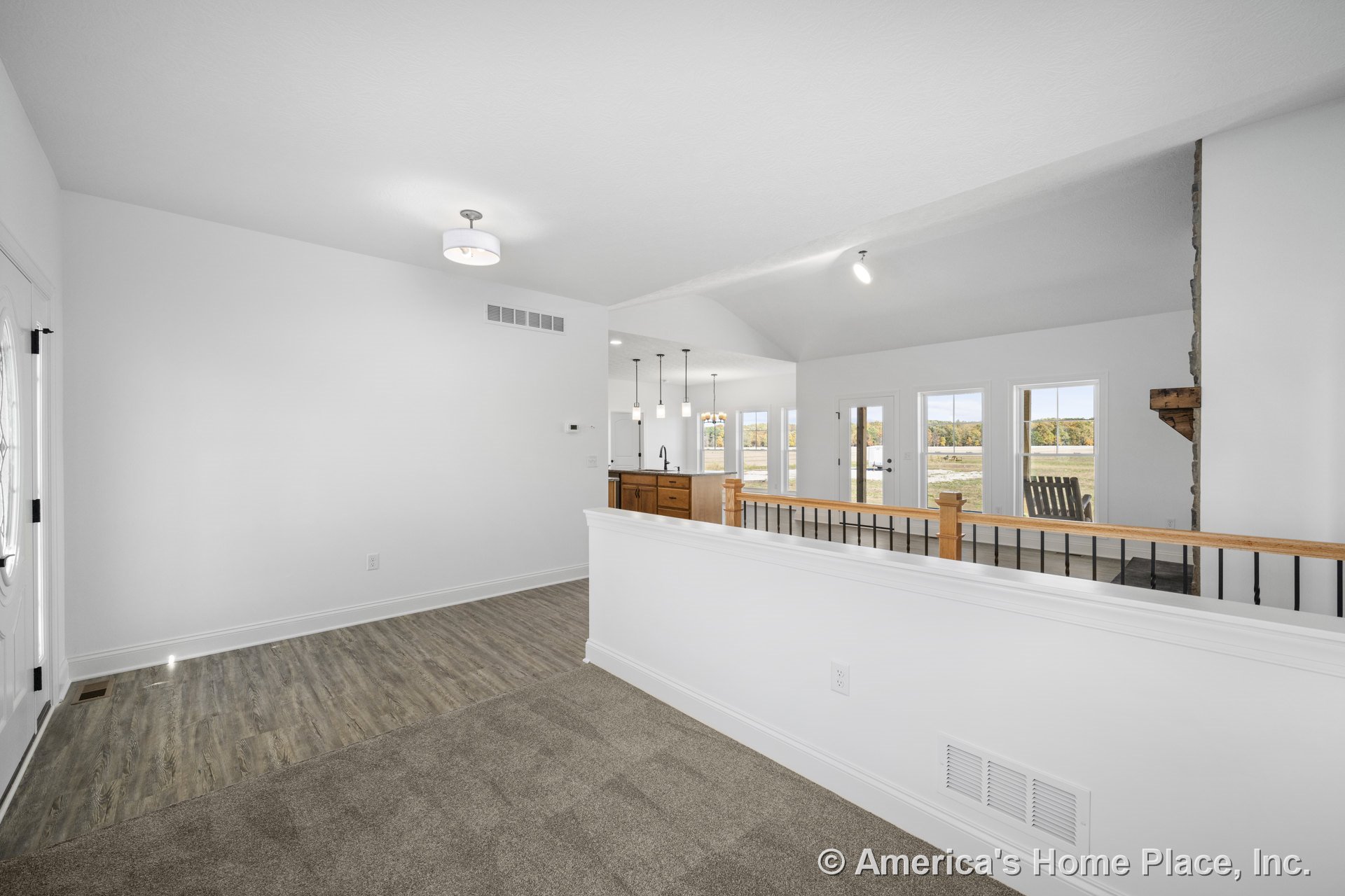 Open floor plan with carpeted foyer transitioning to wood-look vinyl flooring, white painted trim throughout, expansive window wall offering outdoor views, stone fireplace with