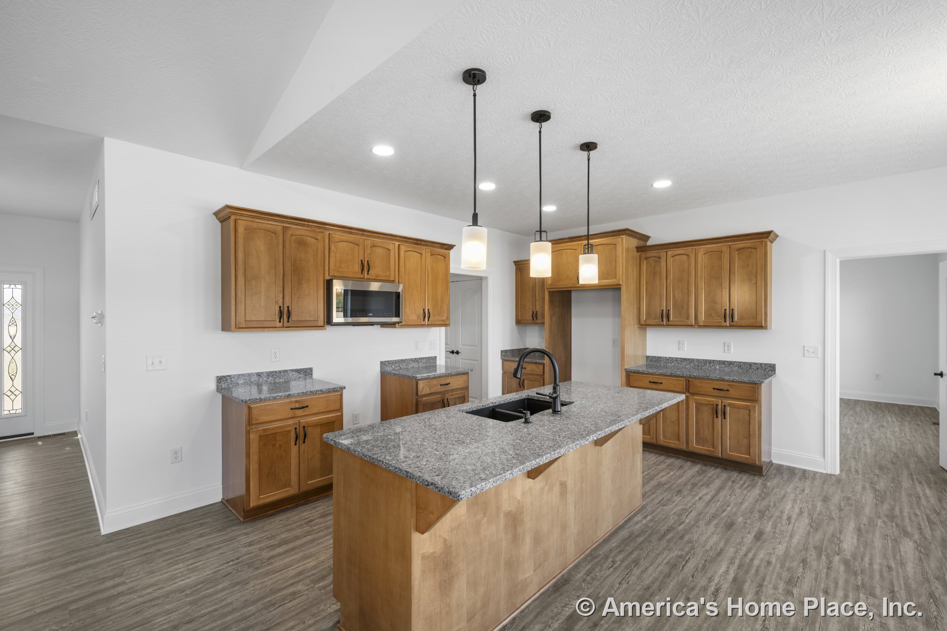 Wood cabinetry kitchen with granite countertops, central island under pendant and recessed lighting, built-in microwave, double sink, vinyl plank flooring, and modern trim in open