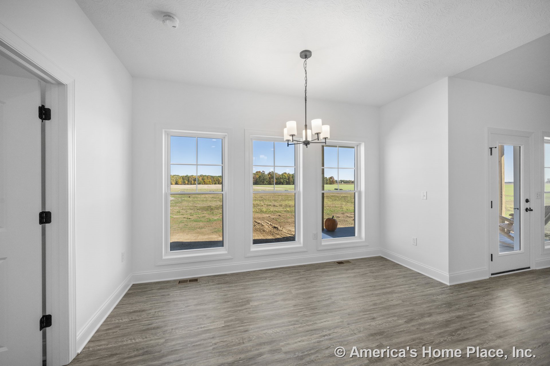 Dining area with triple window wall, glass exterior door, white trim and baseboards, wood-look vinyl flooring, modern chandelier, and smooth white ceiling.