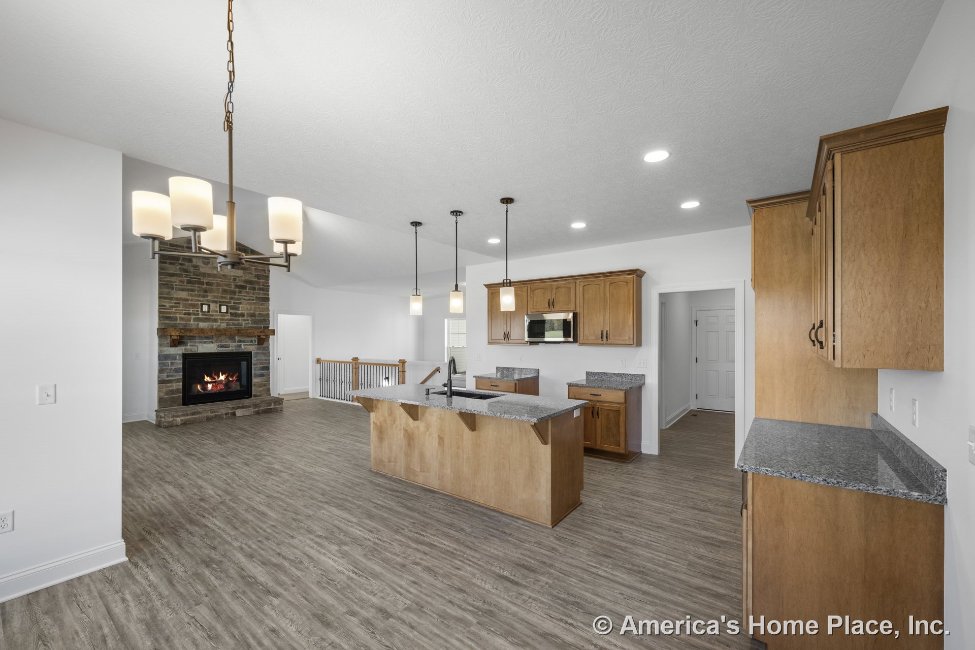 Open concept kitchen and living area with wood cabinetry, granite countertops, stone fireplace with mantel, pendant and recessed lighting, vinyl plank flooring, built-in microwave
