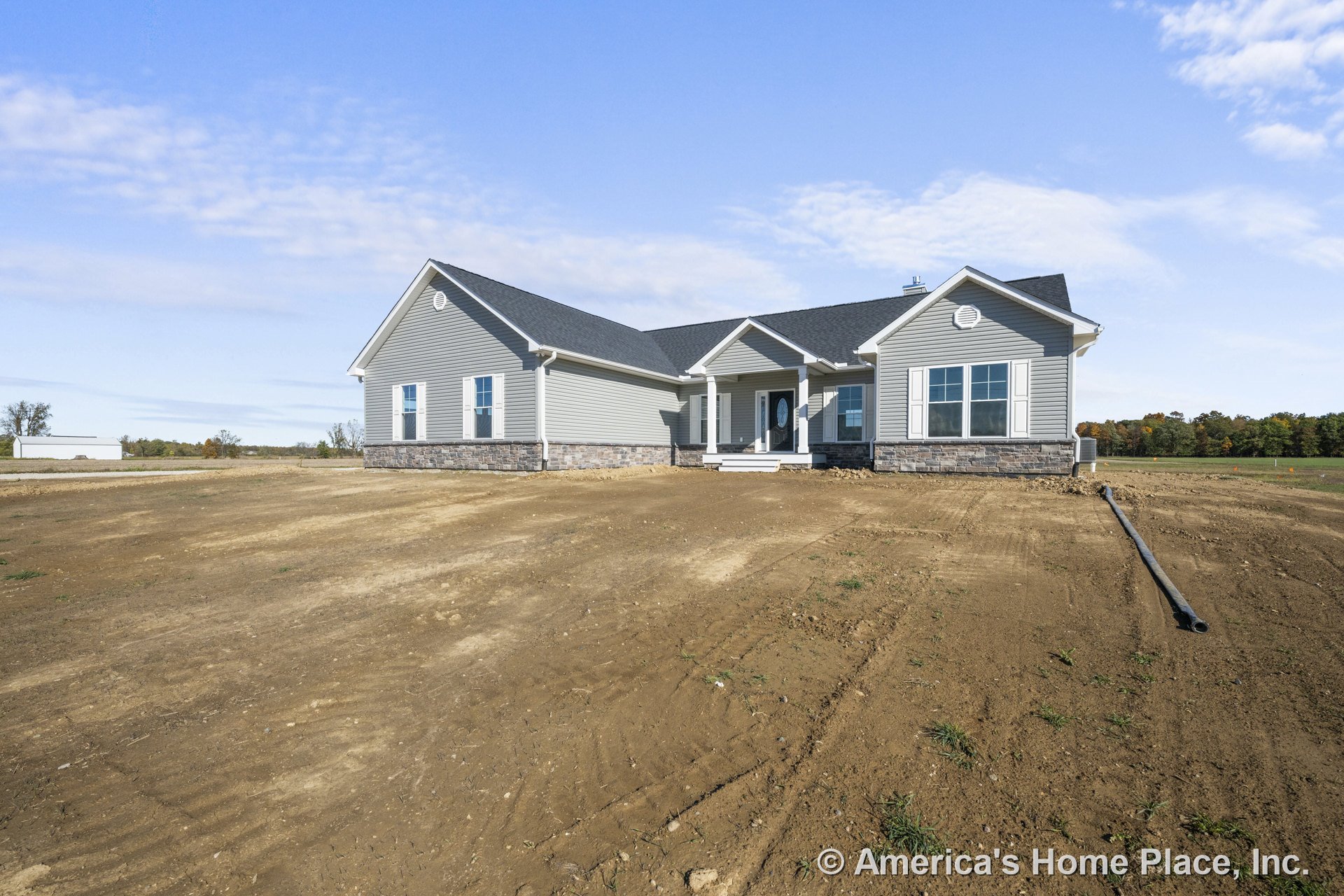 Gray vinyl siding ranch-style home with stone veneer foundation, covered front porch supported by white columns, double-hung windows with white trim, gray shingle roof, and